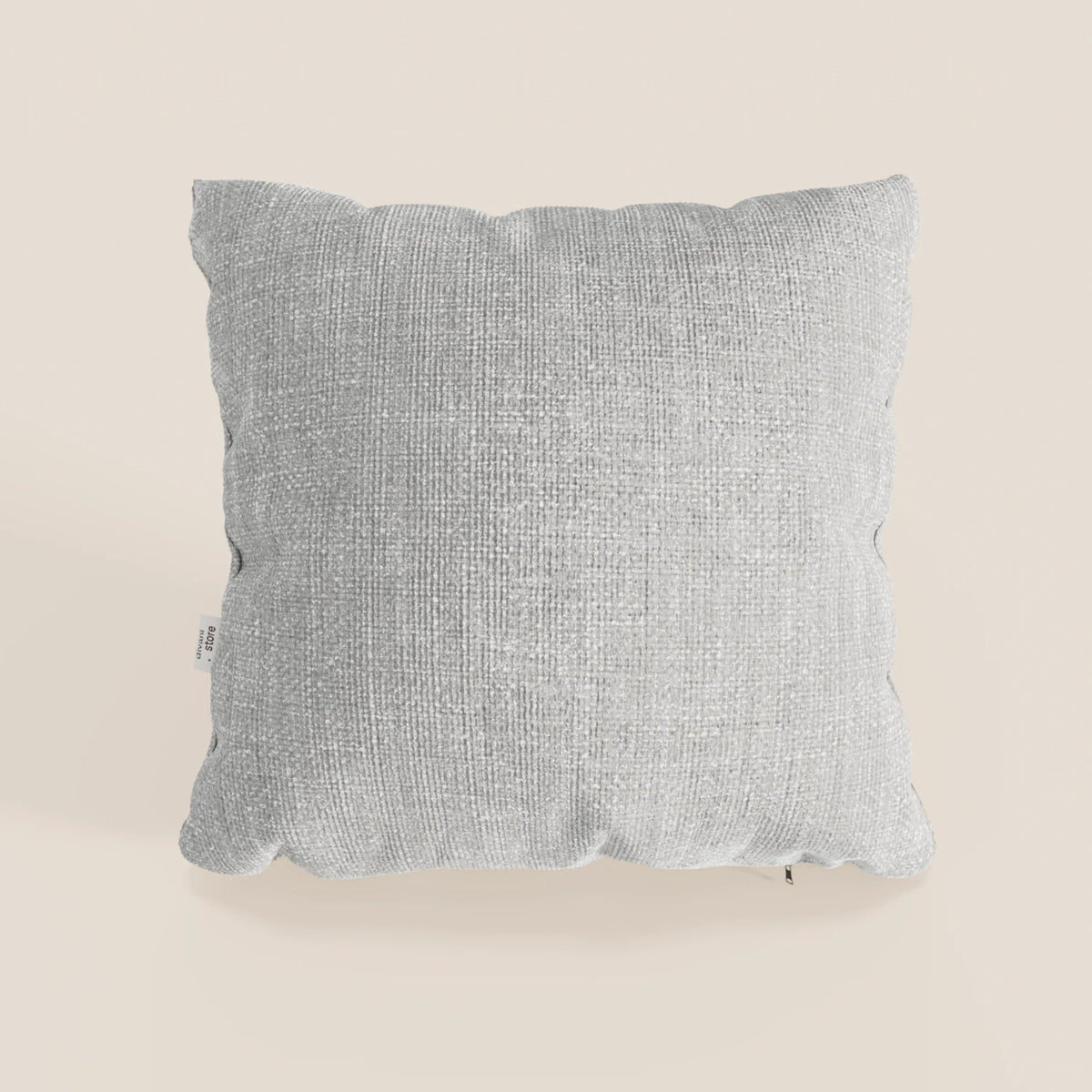 Il cuscino Lyon 45x45 cm di divitt.sbs, in intrecciato impermeabile T06 grigio, è caratterizzato da bordi morbidi e arrotondati e da una piccola etichetta laterale bianca, su sfondo bianco sporco.