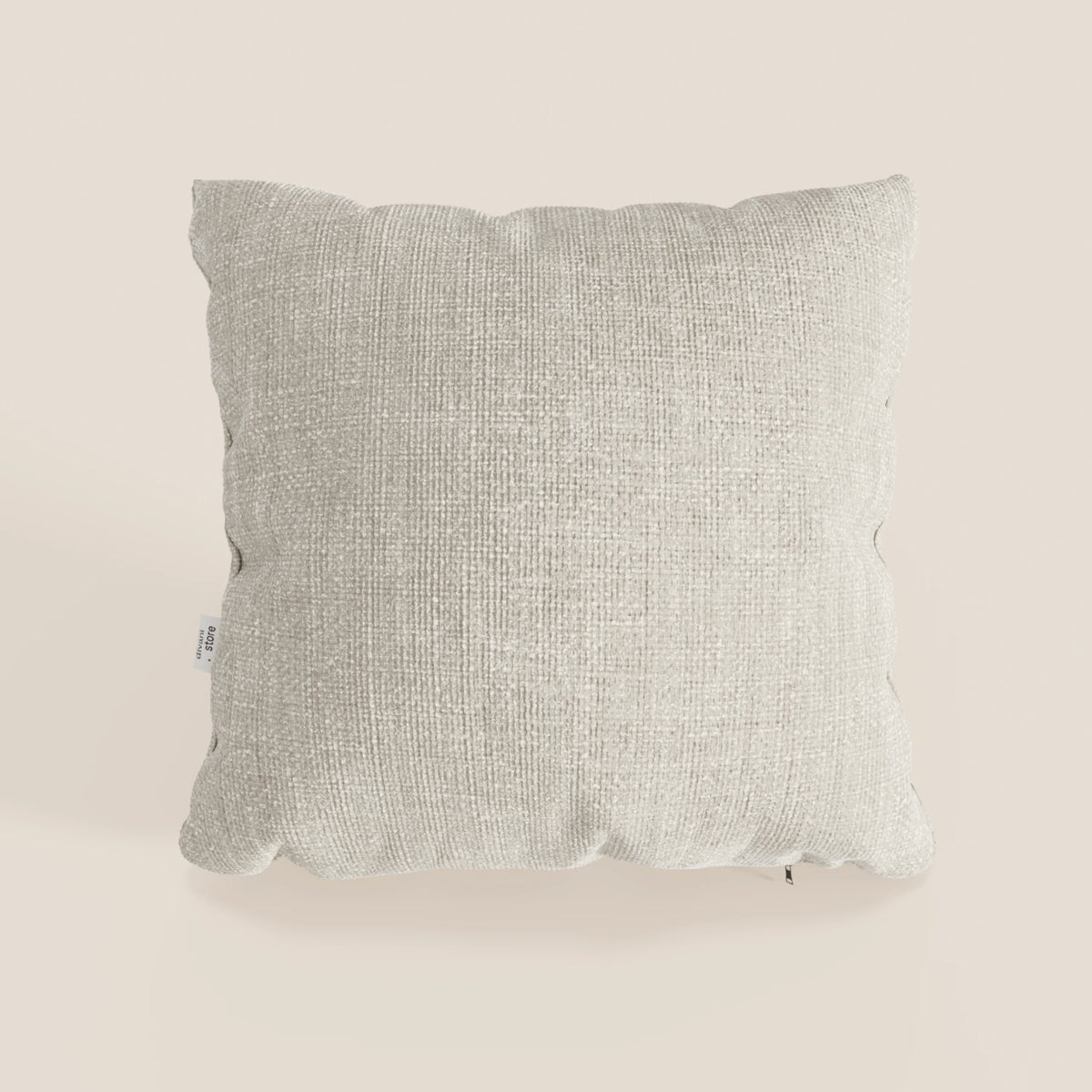 Il cuscino Lyon 45x45 cm di divitt.sbs, in morbido tessuto impermeabile T06 panna, si trova su uno sfondo bianco sporco. Presenta un motivo sottile, una piccola etichetta di cucitura bianca e ombre delicate sotto il cuscino decorativo.