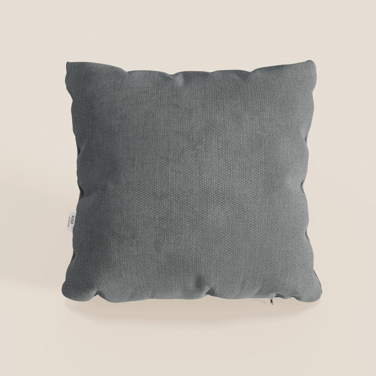 Il cuscino Miami di divitt.sbs, in morbido tessuto impermeabile T14 grigio antracite (45x45 cm), presenta una texture sottile, cuciture a vista, bordi leggermente arrotondati e una piccola etichetta bianca, su sfondo beige chiaro.