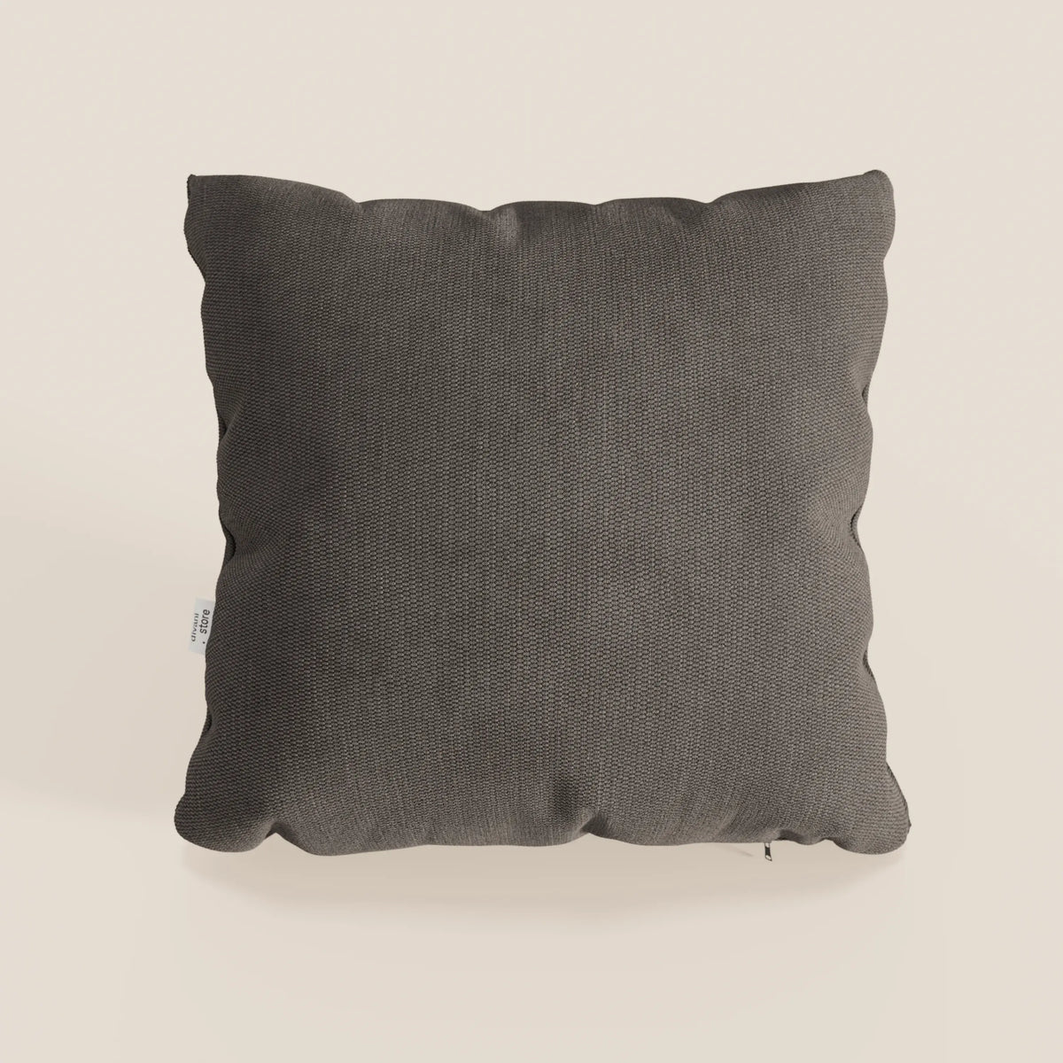 Il cuscino Miami di divitt.sbs, nel formato 45x45 cm T14 marrone, è caratterizzato da un tessuto morbido impermeabile, una texture sottile, angoli arrotondati e una targhetta bianca per un look semplice e moderno su uno sfondo beige chiaro.