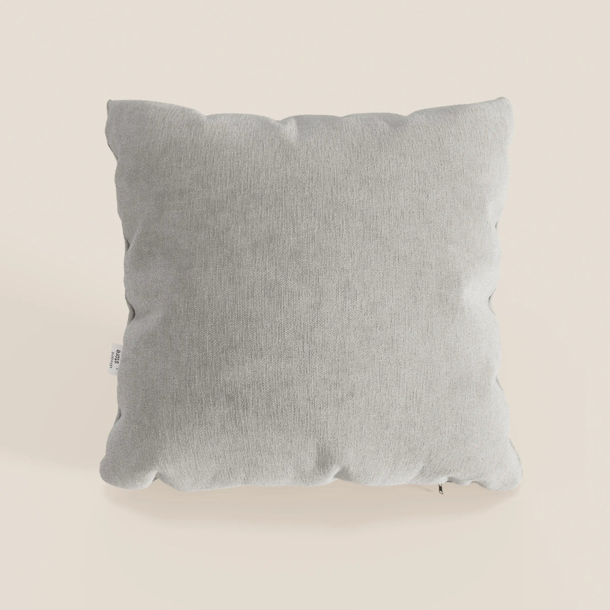 Un cuscino Bolero quadrato grigio chiaro di divitt.sbs si trova su uno sfondo beige chiaro. Realizzato in morbido tessuto T31 antimacchia, impermeabile e non restringente, presenta angoli leggermente arrotondati e una piccola etichetta in tessuto sul lato sinistro.