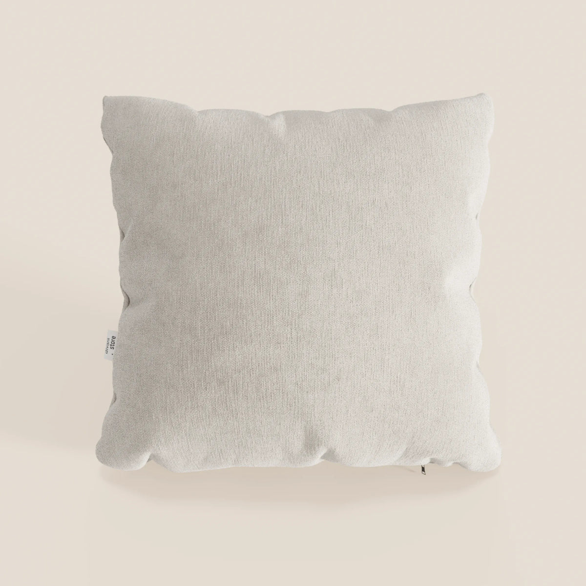 Il cuscino Bolero di divitt.sbs è un cuscino quadrato di colore grigio chiaro in morbido tessuto T31 antimacchia, impermeabile e non restringente. Presenta una texture sottile, angoli smussati e una piccola etichetta bianca sul lato sinistro.