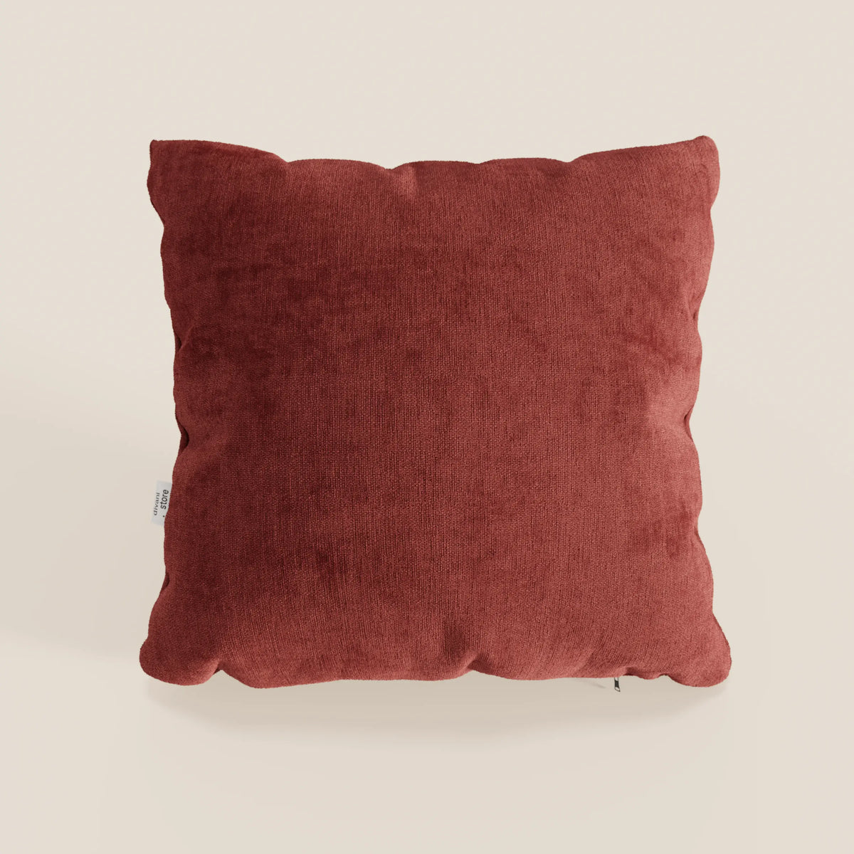 Il cuscino Bolero di divitt.sbs, di colore rosso ruggine, è caratterizzato da un design quadrato e felpato, con un tessuto T31 morbido, antimacchia, impermeabile e non restringente. Ha angoli leggermente arrotondati e una piccola etichetta bianca sul bordo sinistro.