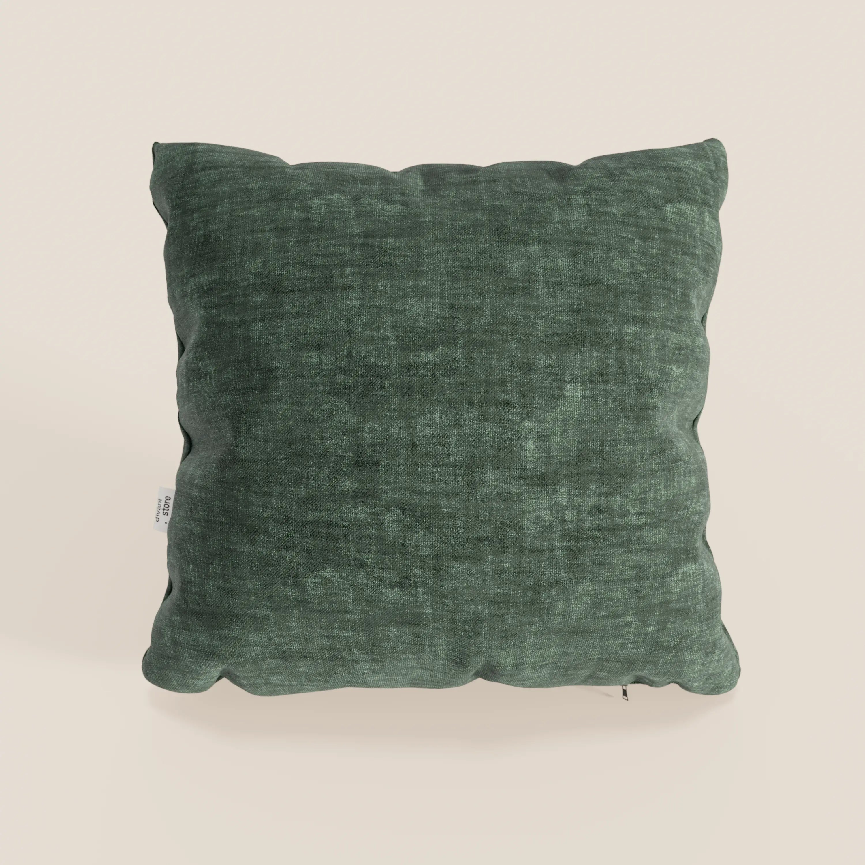 Un cuscino quadrato Sofia verde scuro di divitt.sbs, in morbido velluto antimacchia e impermeabile (Easy Clean T35), poggia su una superficie beige chiaro, con un aspetto abbondante e una leggera piega e una piccola etichetta bianca sulla cucitura sinistra.