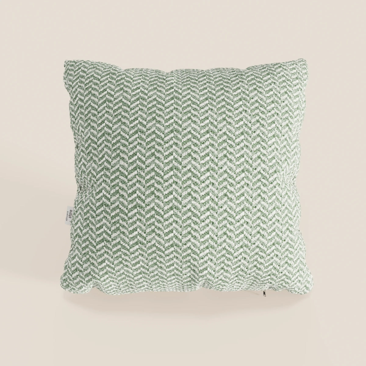 Il cuscino Sorrento 45x45 in lino di divitt.sbs è un morbido cuscino quadrato in lino beige chiaro, con un motivo a spina di pesce verde e bianco e una piccola etichetta in tessuto, parte della collezione Eleganza Naturale.