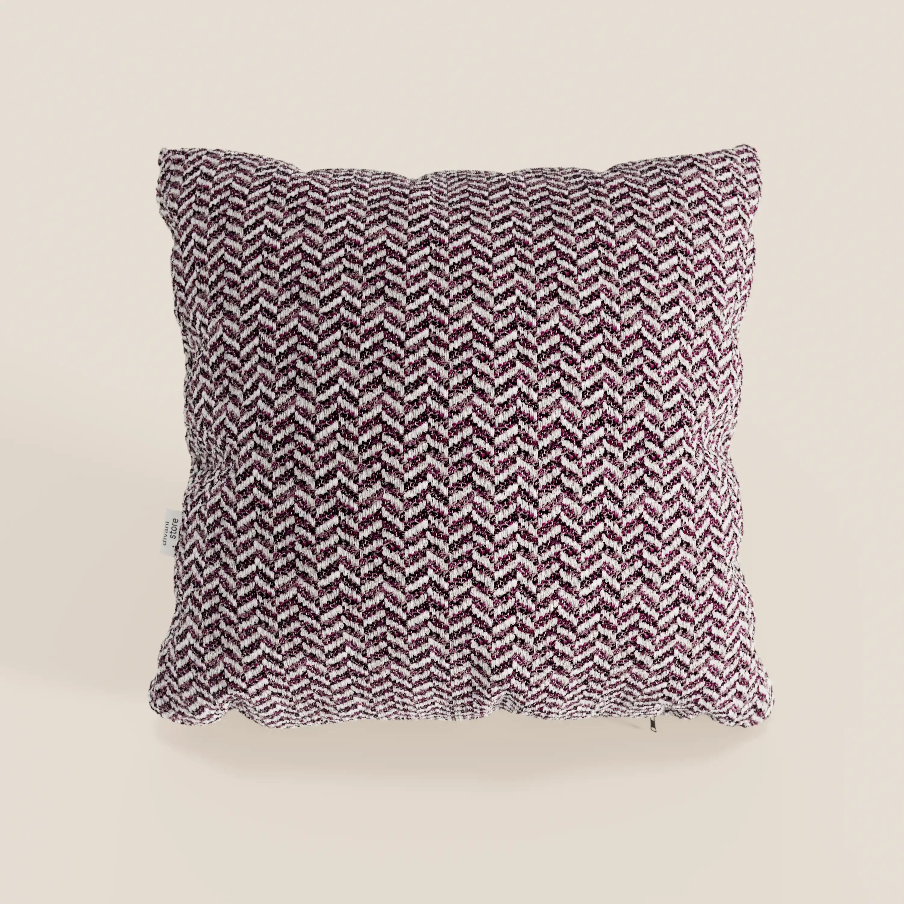 Il cuscino Sorrento 45x45 in lino di divitt.sbs è un cuscino quadrato con un motivo a zig-zag in rilievo nei toni del viola scuro e del bianco su fondo beige chiaro, ispirato al design Nautilus. Presenta una piccola etichetta bianca sul lato che aggiunge un tocco di stile.