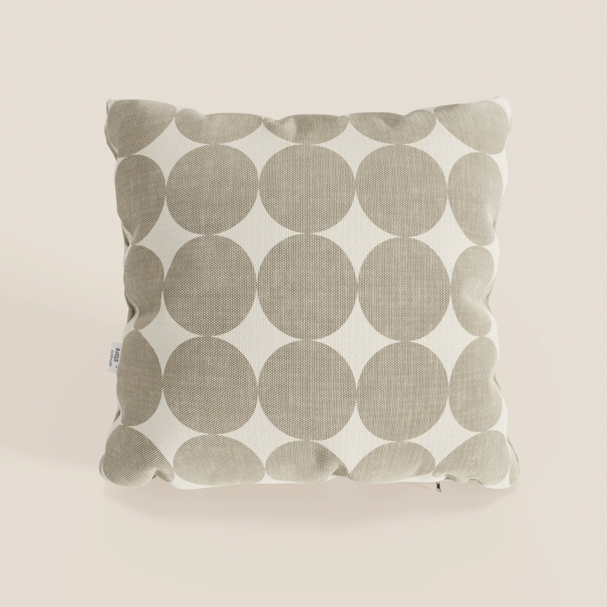 Il cuscino Dot cuscini geometrici di divitt.sbs è un cuscino quadrato in tessuto idrorepellente beige, con motivo geometrico a cerchi bianchi, superficie morbida e strutturata, cuciture a vista ed etichetta in tessuto sul bordo sinistro.
