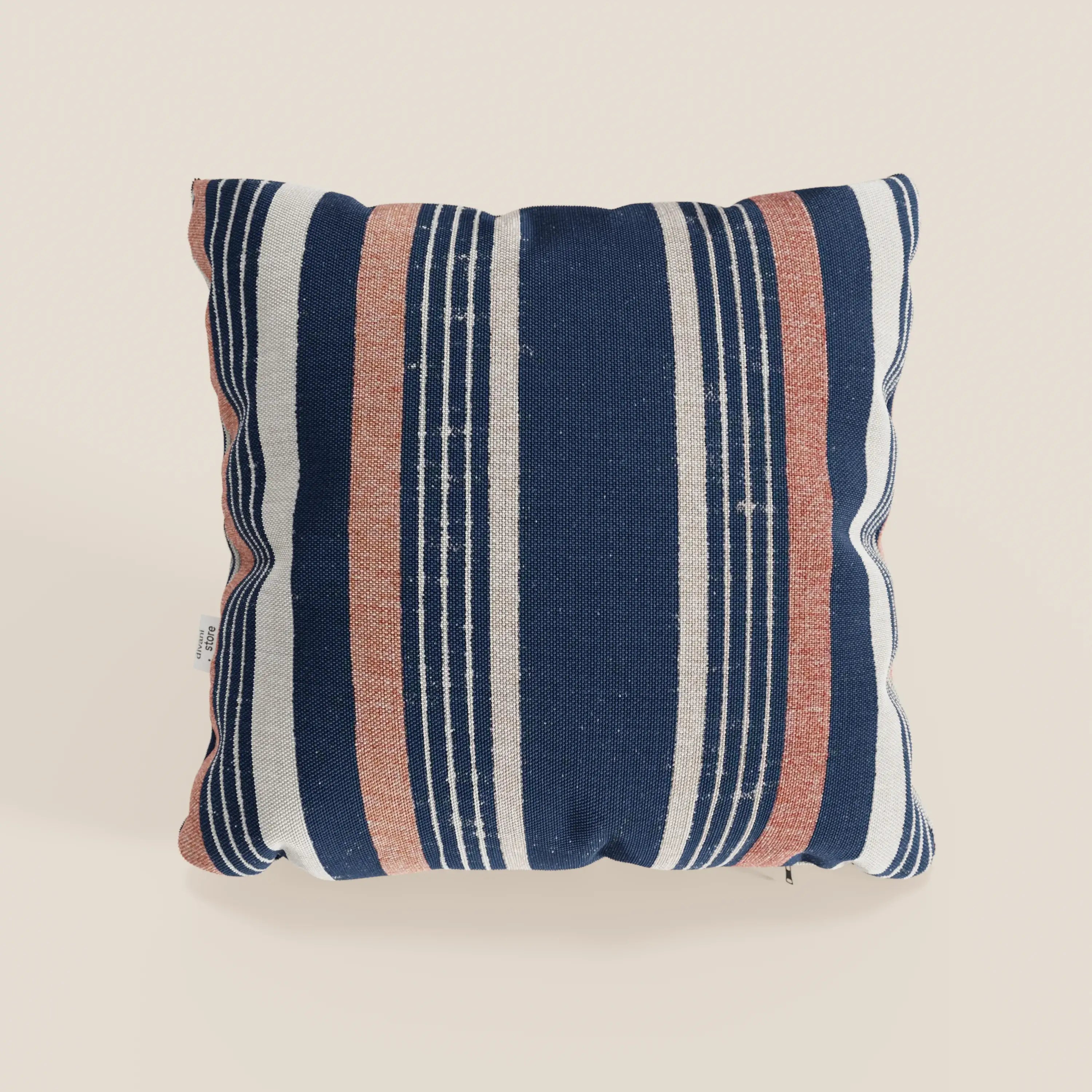Il cuscino Line 45x45 cm di divitt.sbs è caratterizzato da una fantasia rigata in tessuto impermeabile, con righe alternate blu navy, bianche e arancione ruggine. Disponibile in due varianti di colore arancione, su sfondo chiaro.