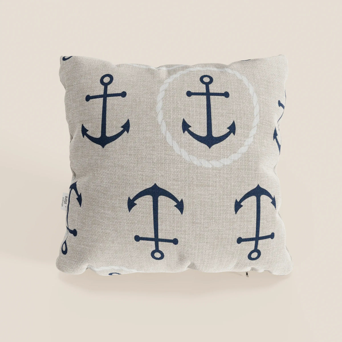 La collezione di cuscini Nautilus di divitt.sbs presenta un cuscino quadrato beige in tessuto impermeabile, con ancore nautiche blu scuro, una delle quali incorniciata da una corda bianca, per un arredamento marino di stile. Esposto su uno sfondo semplice e chiaro.