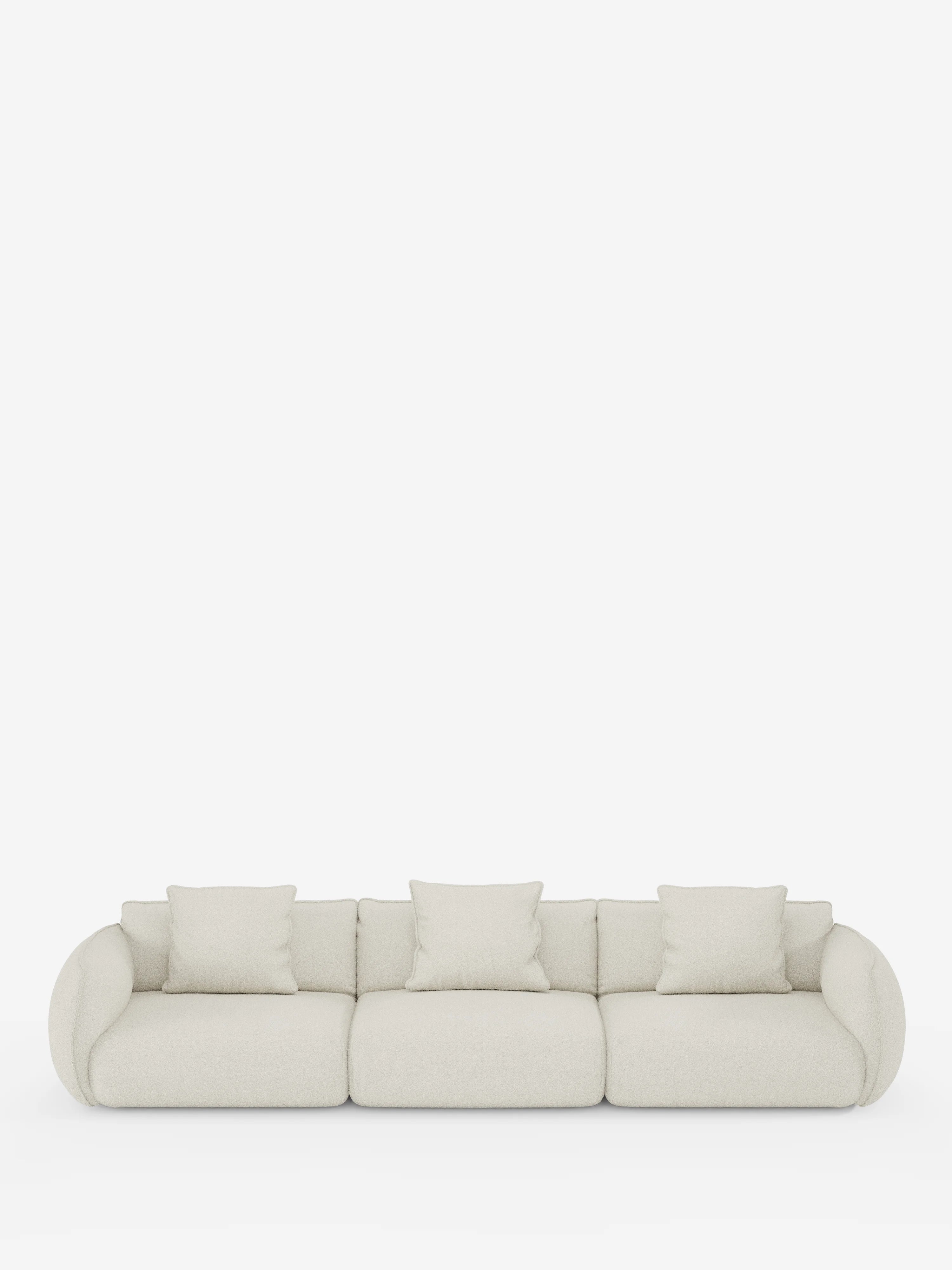 Un moderno divano modulare Nimbus a 3 posti di divitt.sbs, rivestito in tessuto T33 effetto cotone resistente alle macchie, color beige chiaro, caratterizzato da braccioli arrotondati e quattro cuscini quadrati coordinati, su uno sfondo bianco a tinta unita.