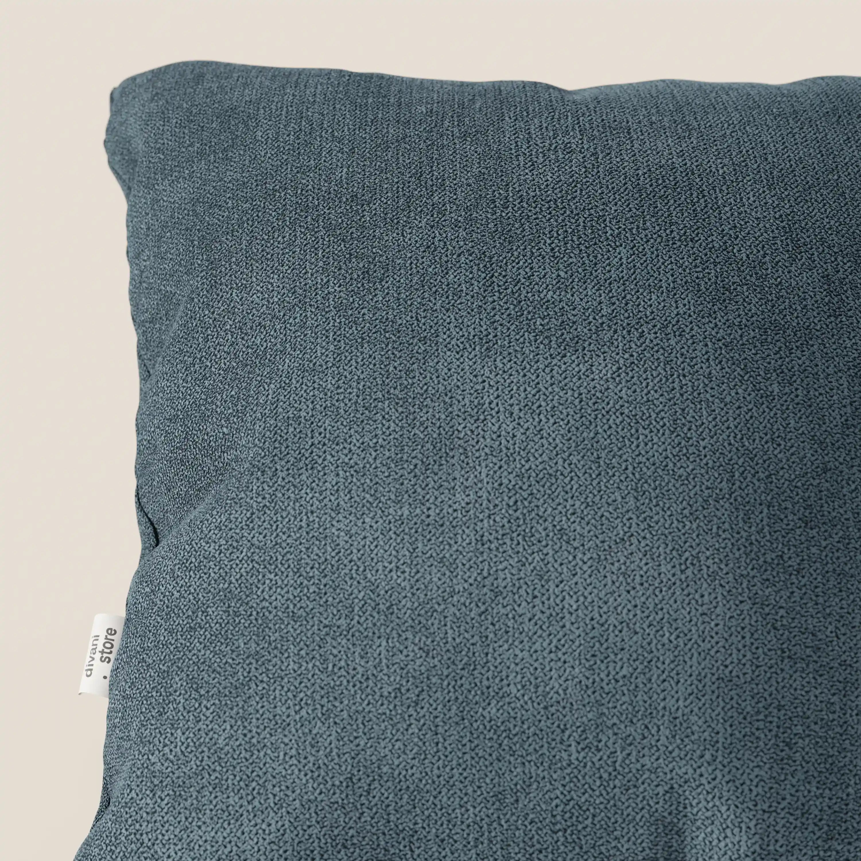 Primo piano del cuscino Destiny 45x45 cm di divitt.sbs in tessuto morbido impermeabile T02 petrolio, disponibile in vari colori, con fodera lavabile e una piccola etichetta bianca a sinistra, su sfondo beige chiaro.
