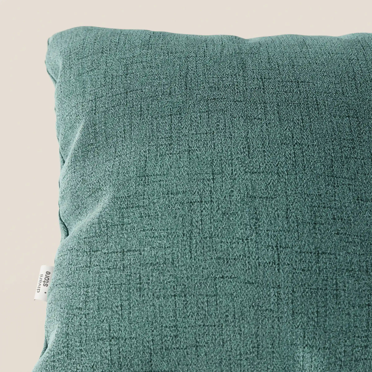 Primo piano del cuscino Felis 45x45 cm in T03 verde acqua di divitt.sbs, realizzato in morbido tessuto idrorepellente con una sottile trama a griglia e una piccola etichetta laterale bianca, su uno sfondo beige chiaro.