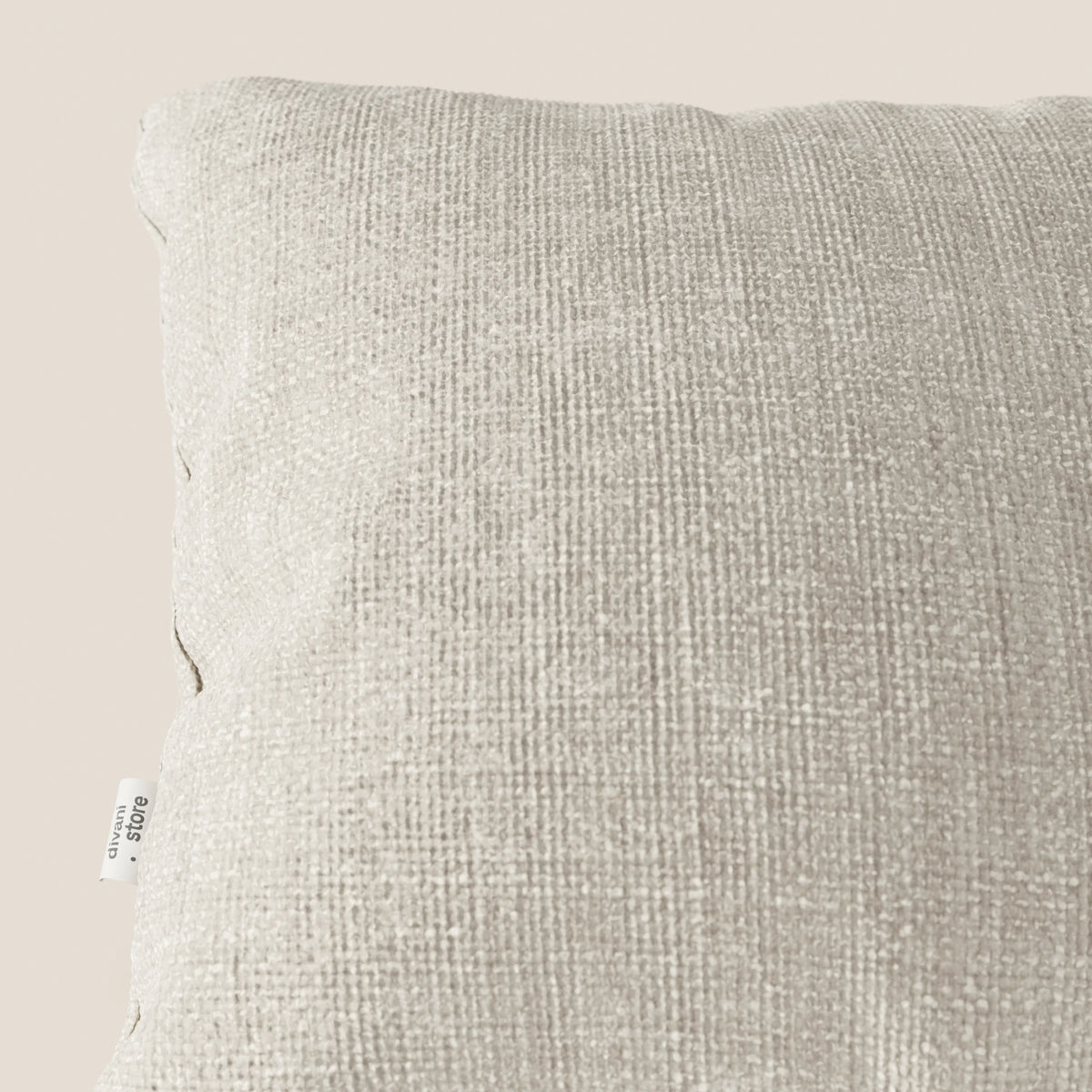 Primo piano del cuscino Lyon 45x45 in panna T06 di divitt.sbs, realizzato in morbido tessuto impermeabile intrecciato. Su uno sfondo crema chiaro, le cuciture sul bordo e la targhetta bianca ne evidenziano la finitura di pregio.