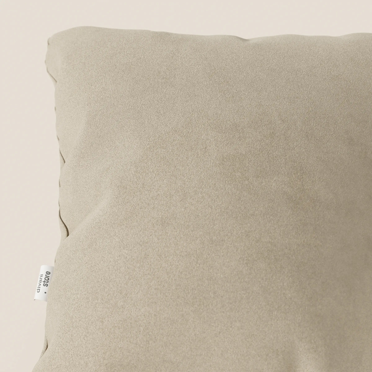 Primo piano dell'angolo superiore sinistro del cuscino Jazz 45x45 cm in microfibra tecnica smacchiabile T11 beige di divitt.sbs, caratterizzato da una texture morbida e liscia e da una piccola etichetta in tessuto bianco con testo nero sulla cucitura.