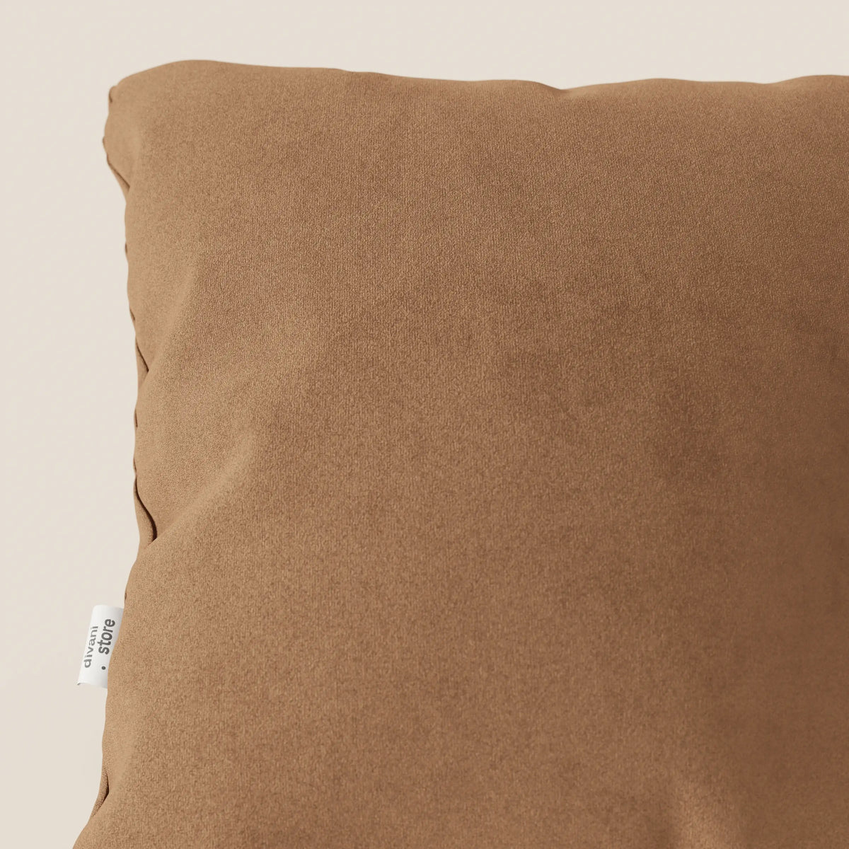 Primo piano del cuscino Jazz di divitt.sbs, in T11 cuoio smacchiabile microfibra. Il cuscino quadrato presenta una consistenza morbida e un'etichetta in tessuto bianco sulla cucitura sinistra, su uno sfondo beige chiaro. Solo una parte è visibile.