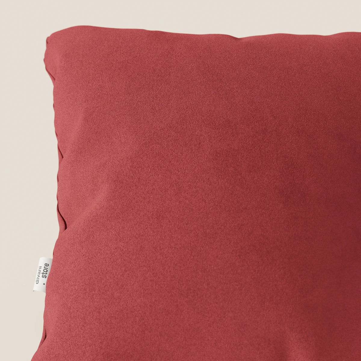 Primo piano del cuscino Jazz di divitt.sbs in microfibra tecnica smacchiabile T11 rosso, caratterizzato da una forma morbida e quadrata con una texture liscia e una piccola etichetta bianca sul lato. Lo sfondo è un semplice color crema chiaro.