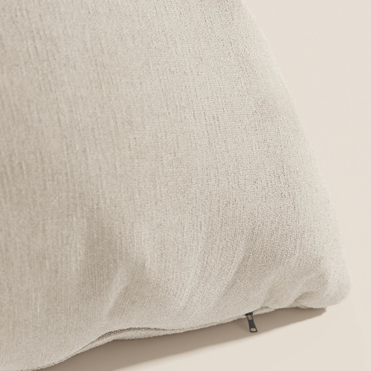 Primo piano del cuscino Bolero di divitt.sbs in beige chiaro su uno sfondo neutro. Realizzato in morbido tessuto T31, resistente alle macchie, impermeabile e non restringente, presenta un sottile motivo intrecciato e una piccola cerniera nera.