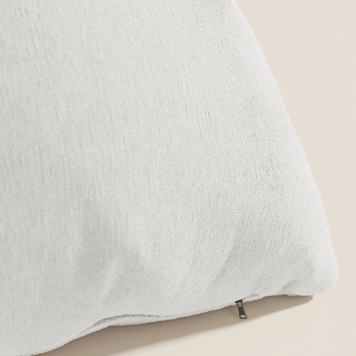 Primo piano dell'angolo di un cuscino Bolero bianco di divitt.sbs, realizzato in morbido tessuto T31 antimacchia, impermeabile e non restringente. Una cerniera nera sulla cucitura mostra il rivestimento sfoderabile. Lo sfondo beige ne sottolinea la consistenza.