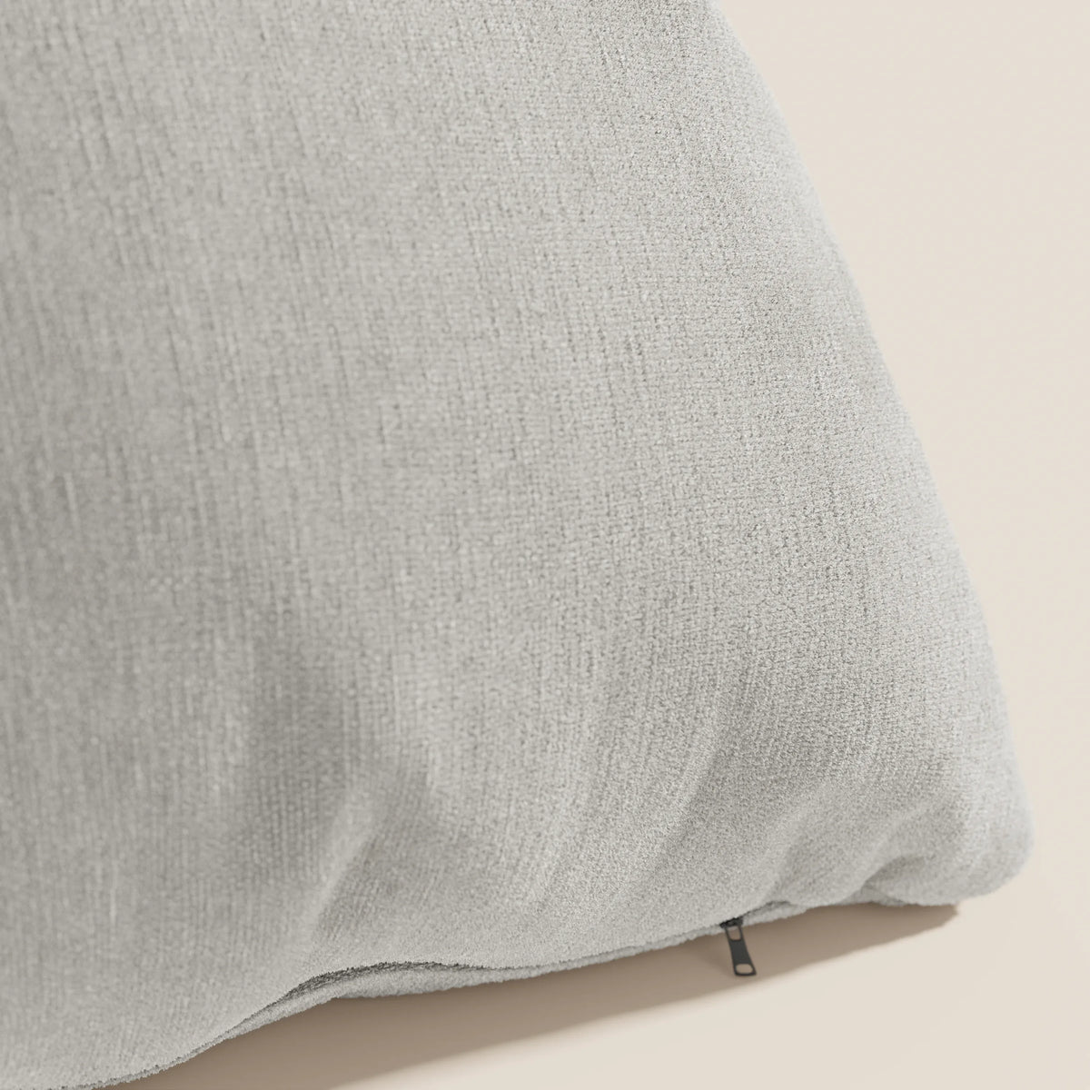 Primo piano del cuscino Bolero di divitt.sbs in grigio chiaro, con tessuto T31 morbido, antimacchia, impermeabile e termoretraibile, sfoderabile, su sfondo beige con trama a vista e tirazip nero.