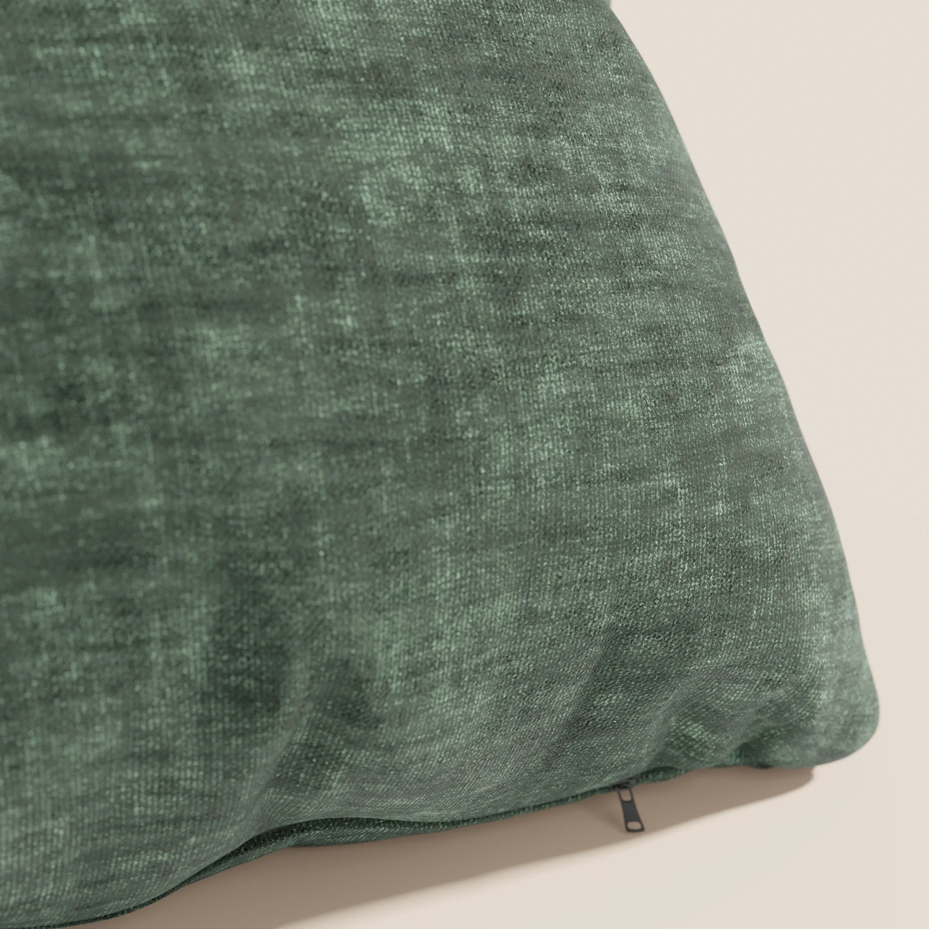 Primo piano del cuscino Sofia di divitt.sbs in verde scuro, realizzato in morbido velluto nuvolato (Easy Clean T35) antimacchia e impermeabile, con texture screziata e cerniera inferiore a vista, su una parete in tinta unita beige chiaro.