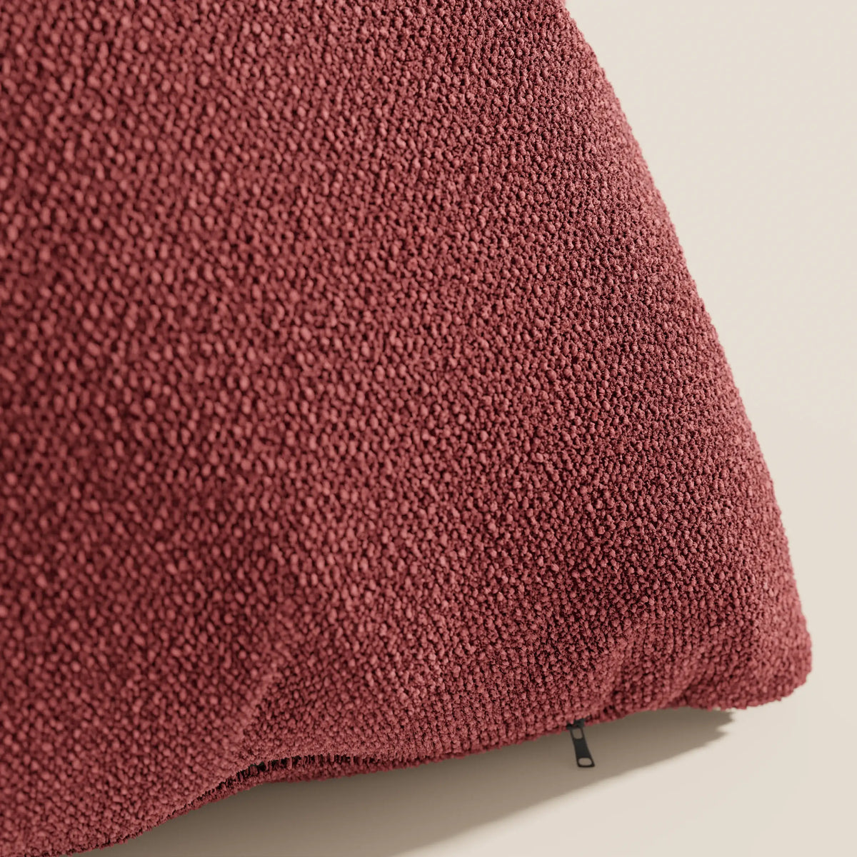 Primo piano del cuscino Lambada bordeaux di divitt.sbs, realizzato in tessuto fresco, antimacchia e impermeabile T33 effetto cotone naturale, con cerniera a vista sul bordo inferiore su sfondo beige chiaro.
