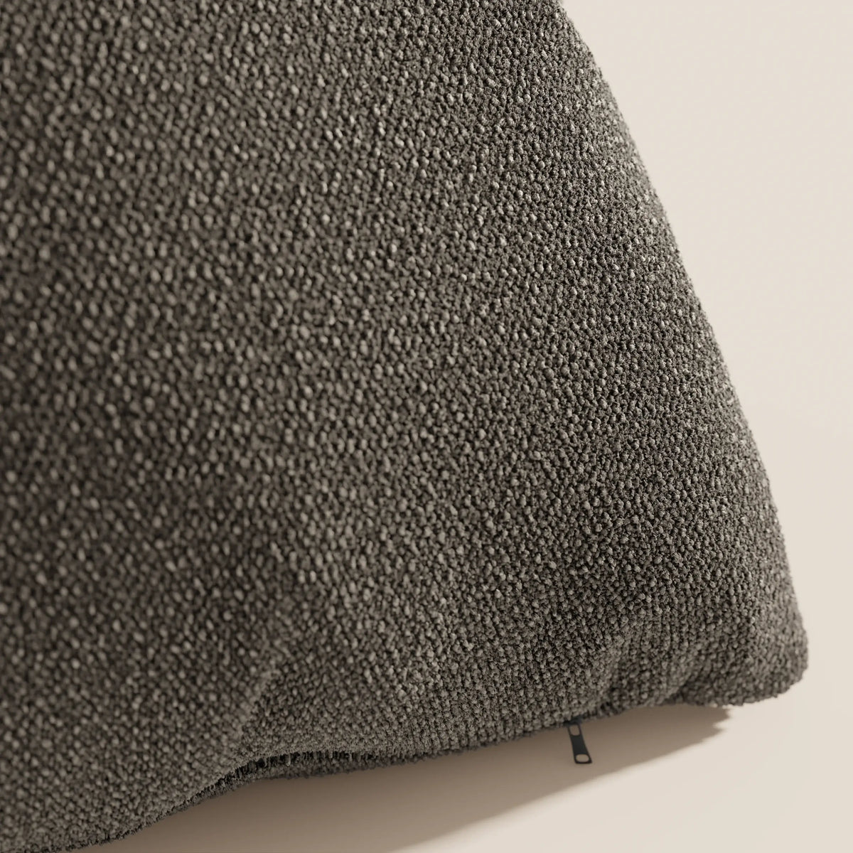 Primo piano del cuscino Lambada grigio scuro di divitt.sbs, realizzato in fresco tessuto naturale simil-cotone (T33) lavabile e impermeabile, caratterizzato da una finitura a ciottoli e arricchito da una piccola etichetta in tessuto nero.