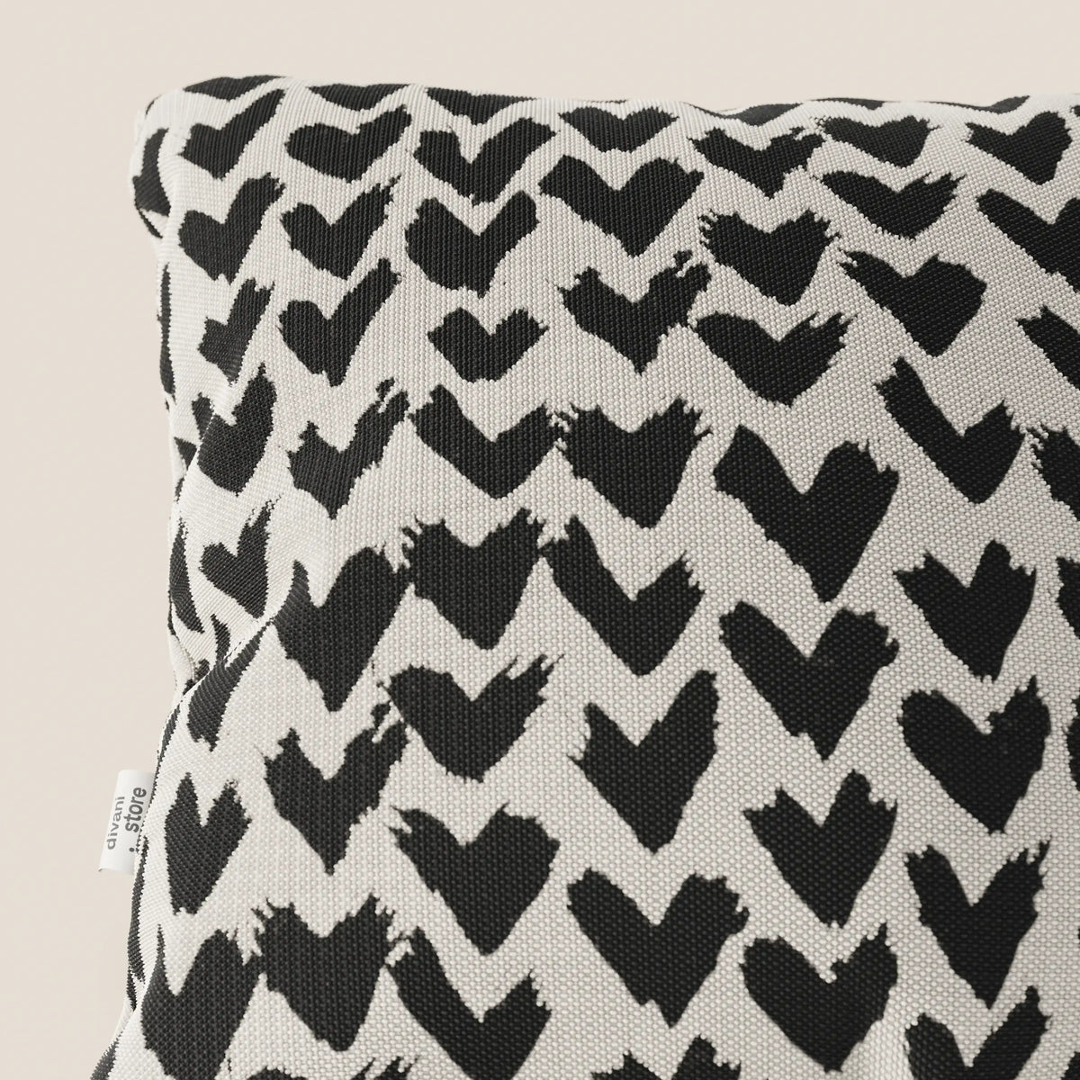 Primo piano dei cuscini geometrici Arrow di divitt.sbs, realizzati in tessuto nero idrorepellente e disponibili in vari colori. Una piccola etichetta bianca sul bordo indica "cotone 100%".