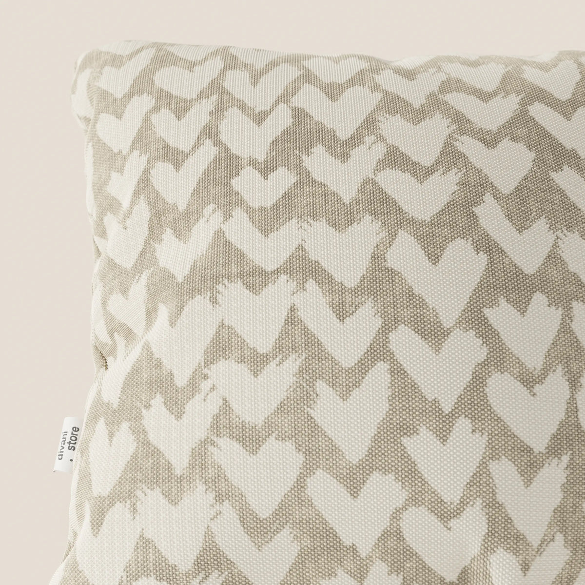Primo piano dei cuscini geometrici divitt.sbs Arrow in beige, caratterizzati da un tessuto strutturato e idrorepellente con un motivo geometrico a cuore. Una piccola etichetta bianca con testo nero appare sul bordo sinistro su uno sfondo beige chiaro.