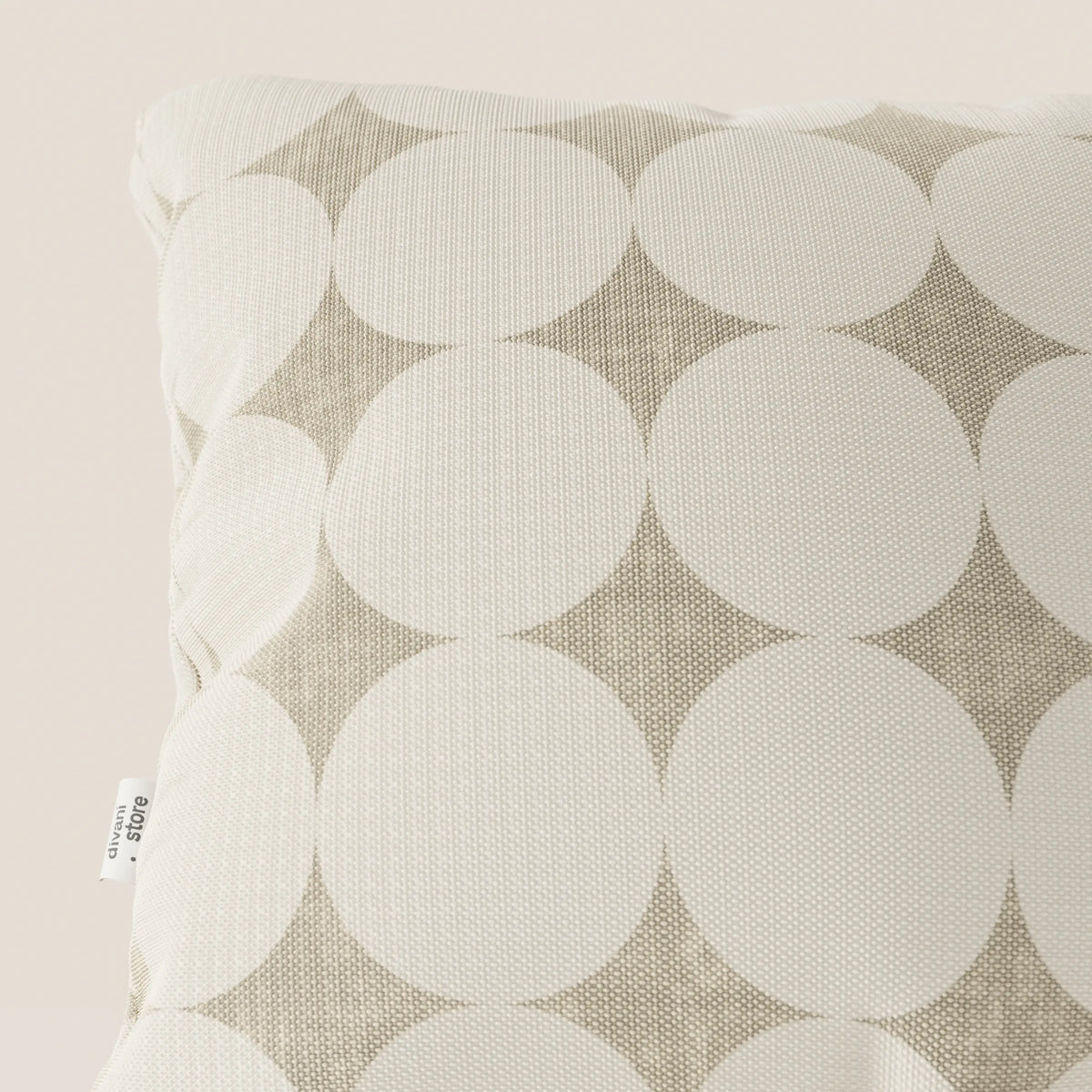 Primo piano del cuscino geometrico Dot di divitt.sbs, che presenta un tessuto idrorepellente bianco con grandi cerchi sovrapposti color crema su sfondo beige e un'etichetta laterale visibile.