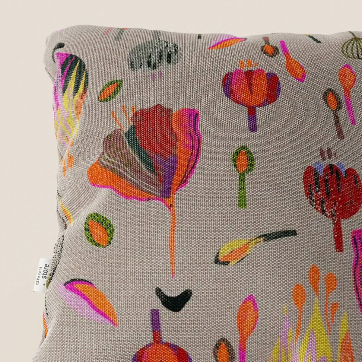 Primo piano del cuscino Joy 45x45 cm di divitt.sbs, caratterizzato da un vivace motivo floreale astratto multicolore su un fresco tessuto di cotone grigio impermeabile. Sul bordo sinistro è visibile una piccola etichetta bianca.