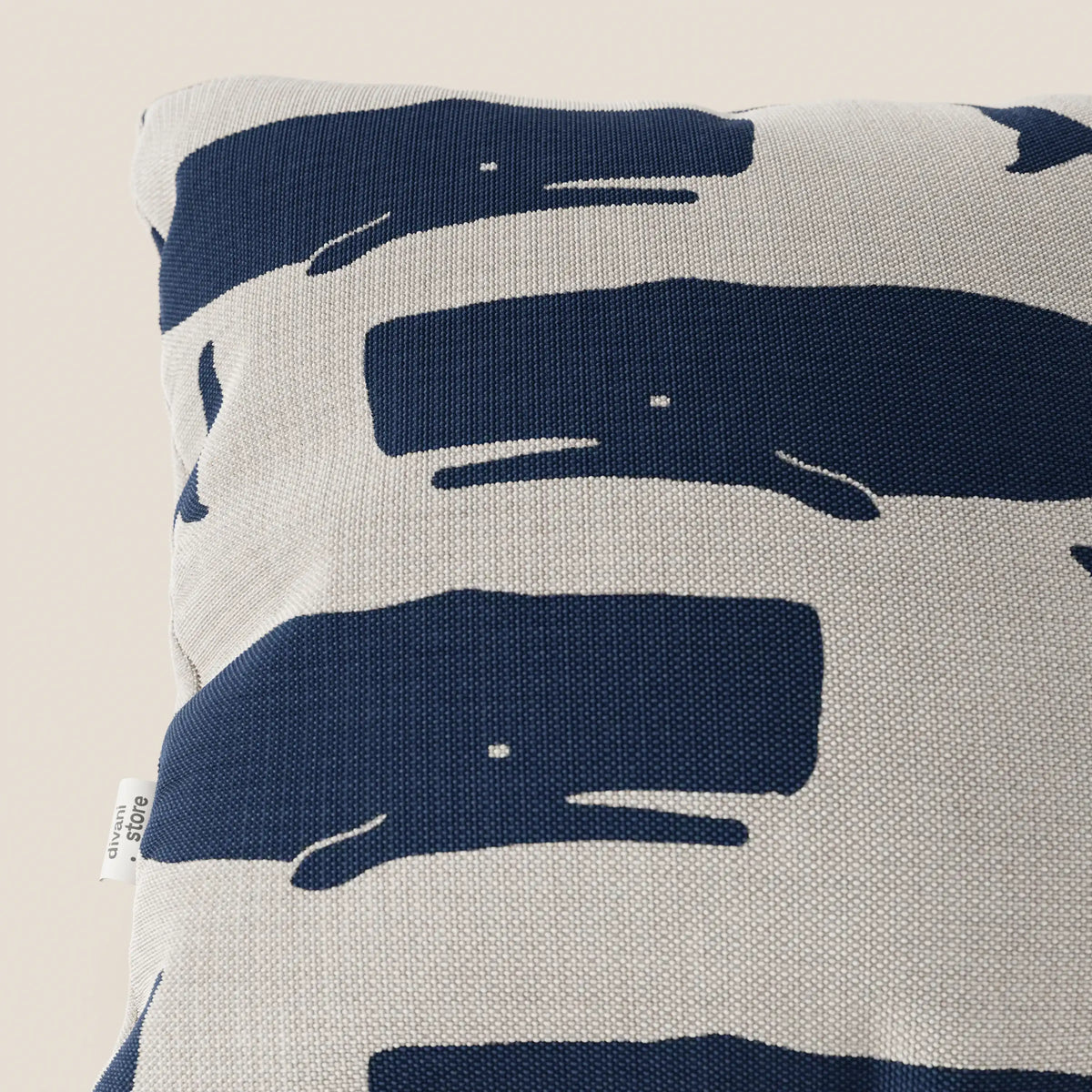 Cuscino quadrato della collezione di cuscini Nautilus di divitt.sbs, caratterizzato da balene astratte di colore blu navy con piccoli occhi bianchi su tessuto impermeabile grigio chiaro e etichetta sul bordo sinistro. Stile marino, ideale per la decorazione.
