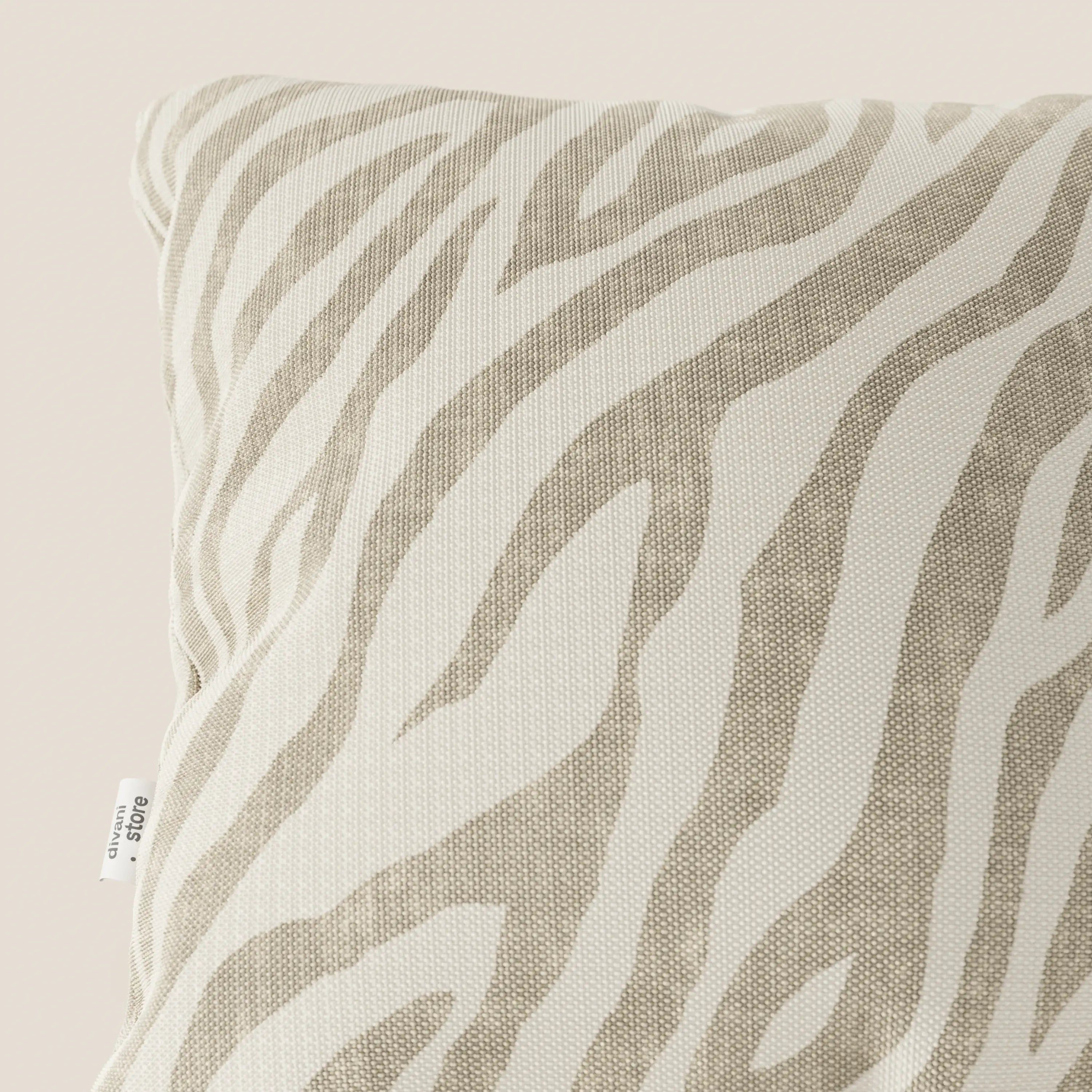 Primo piano di Stripe cuscini geometrici in tessuto Idrorepellente di divitt.sbs, a righe zebrate bianche e beige. Una piccola etichetta in tessuto bianco con testo nero è cucita nella cucitura. Lo sfondo è di un colore chiaro e neutro.