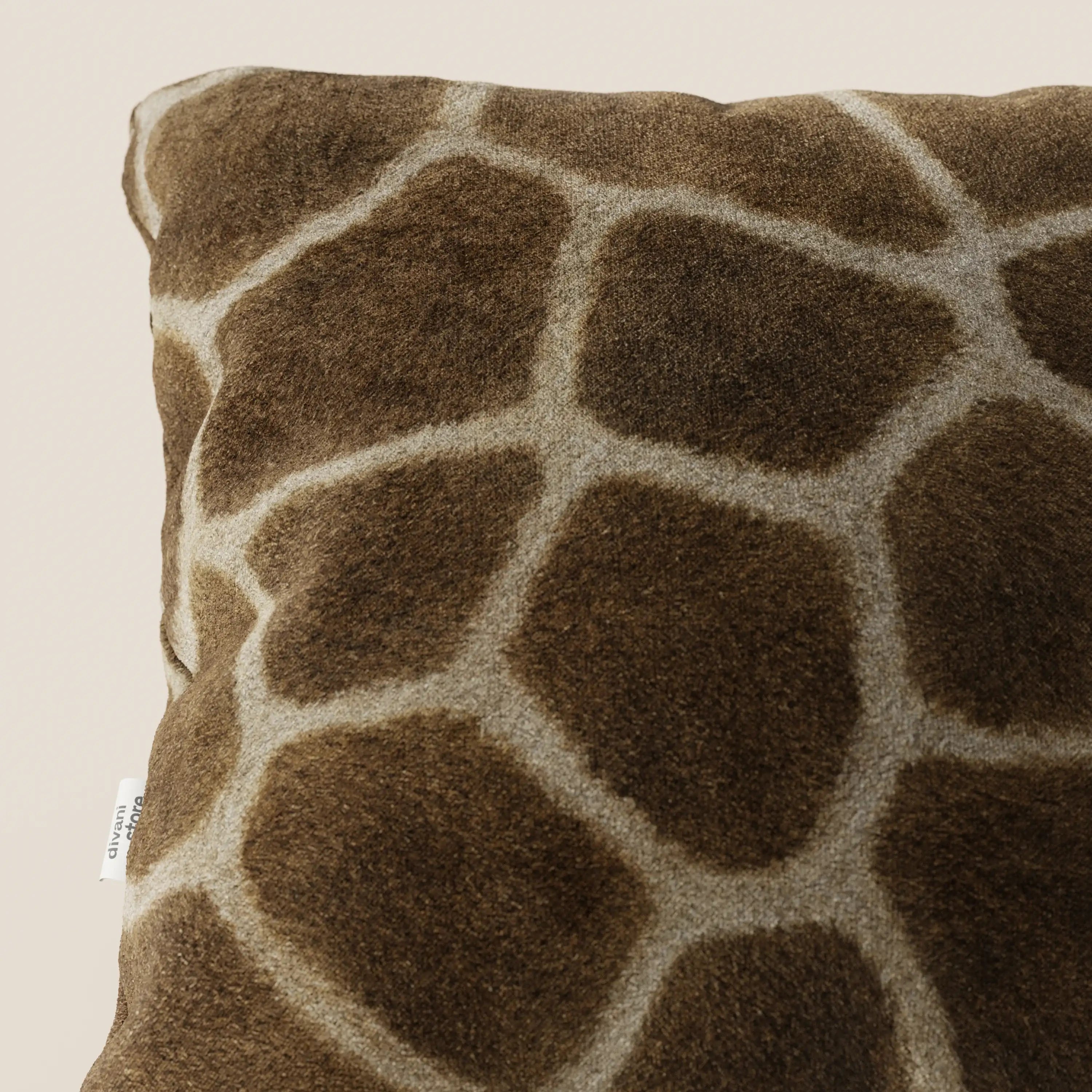 Primo piano del cuscino della collezione Wild in microfibra impermeabile giraffa di divitt.sbs, un cuscino quadrato lavabile con rivestimento in morbida ecopelliccia marrone e stampa giraffa color crema, caratterizzato da una piccola etichetta bianca su sfondo beige chiaro.