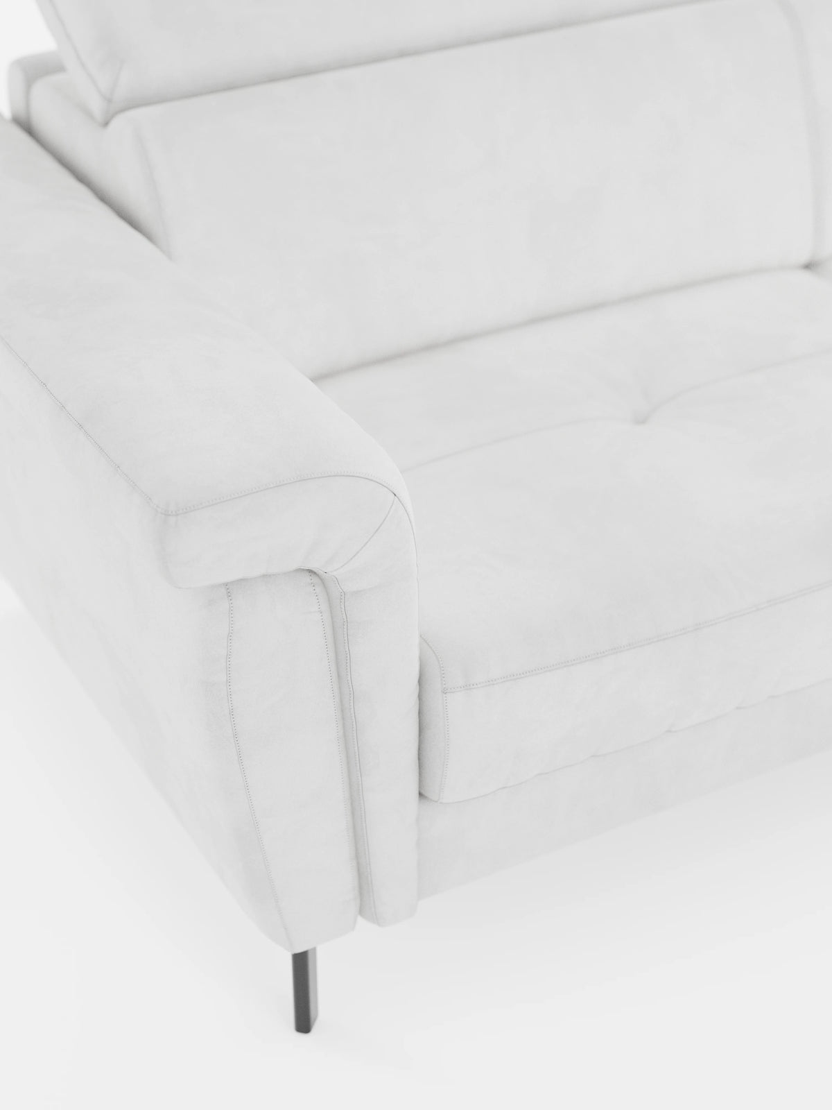 Un primo piano del divano letto di design Capri di divitt.sbs, realizzato in raffinato tessuto T30 effetto velluto resistente alle macchie: si notano un bracciolo, un cuscino di seduta leggermente trapuntato e sottili gambe in metallo nero su sfondo bianco. Il rivestimento è morbido e liscio, dall’estetica minimalista, e si completa con poggiatesta regolabili per un comfort ancora maggiore.