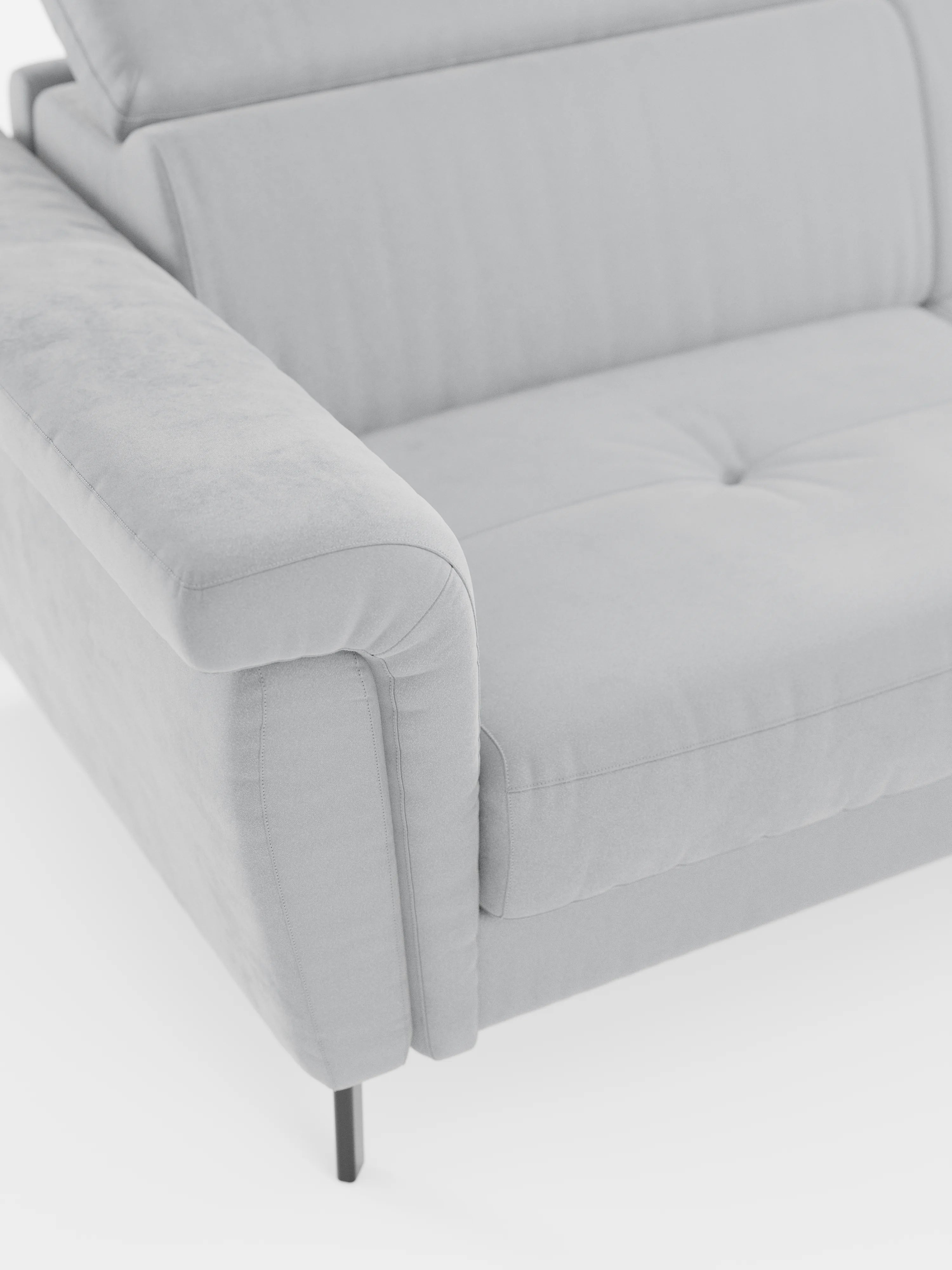 Un primo piano del divano letto di design Capri di divitt.sbs, caratterizzato da un rivestimento grigio chiaro in raffinato tessuto effetto velluto smacchiabile T30, moderni braccioli morbidi e arrotondati, cuscini di seduta trapuntati e sottili piedini alti in metallo nero. Il lato sinistro e parte della zona di seduta sono visibili su uno sfondo bianco, che mette in risalto la raffinata manifattura italiana e i poggiatesta reclinabili.