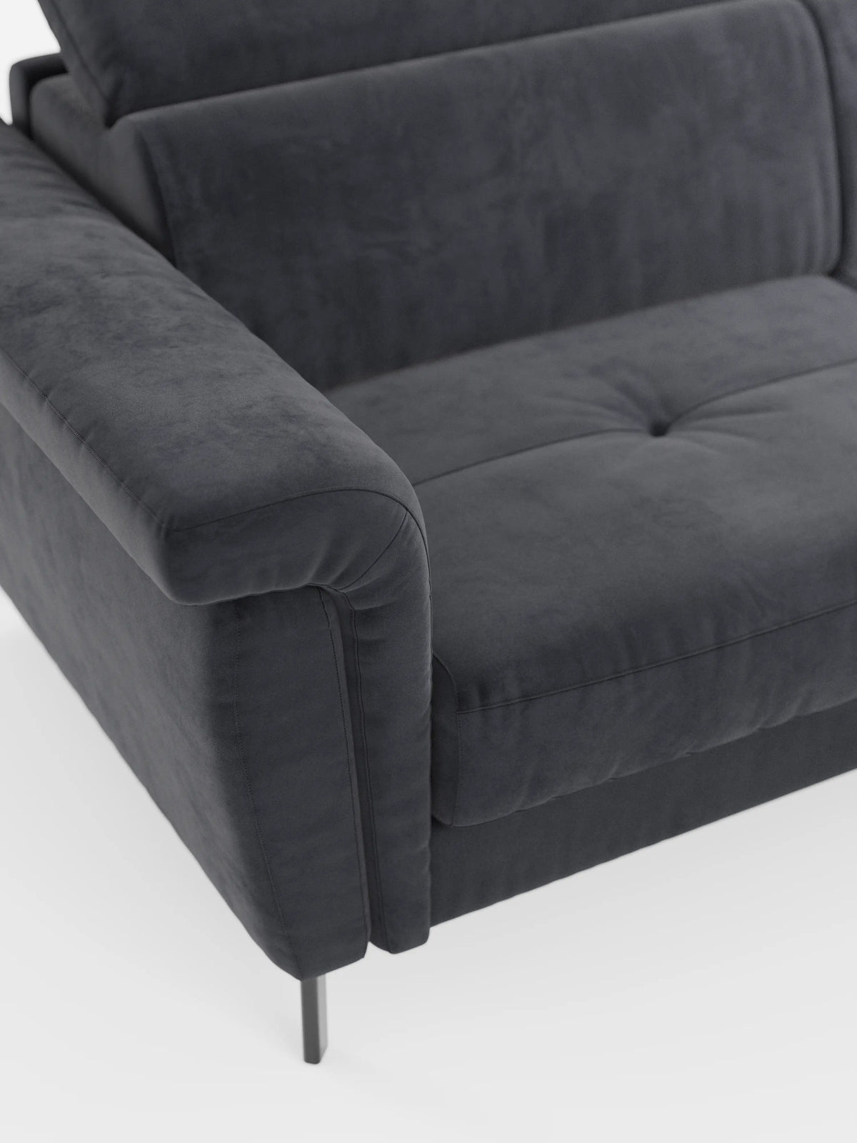 Primo piano del divano letto di design Capri con piedini alti di divitt.sbs, che mette in risalto il bracciolo sinistro, il morbido cuscino di seduta con delicati dettagli trapuntati e l'elegante gamba in metallo. Rivestito in raffinato tessuto effetto velluto smacchiabile T30 dall’aspetto particolarmente morbido e lussuoso, questo moderno divano grigio scuro presenta una superficie vellutata. Lo sfondo è bianco a tinta unita.