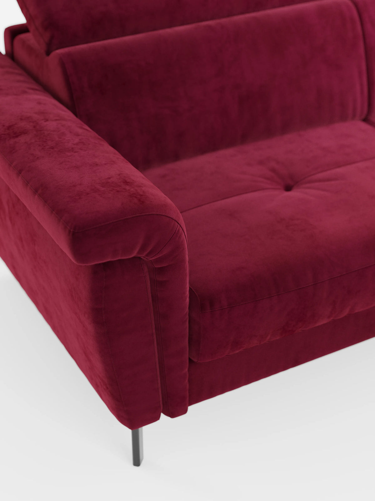 Un primo piano del divano letto di design Capri con piedini alti di divitt.sbs, realizzato in raffinato tessuto effetto velluto antimacchia T30, mette in risalto il bracciolo sinistro, un cuscino di seduta con due bottoni e un'elegante gamba in metallo. Il divano presenta un aspetto morbido e materico con eleganti poggiatesta reclinabili, che risaltano su uno sfondo bianco a tinta unita.