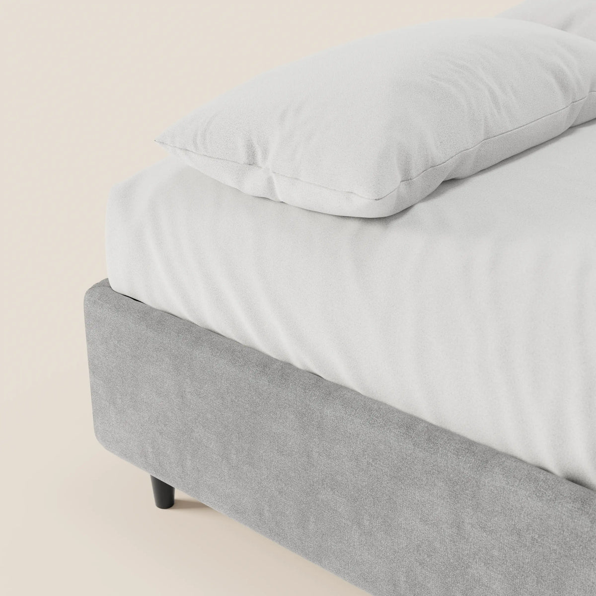 Un primo piano di un letto sommier ERON di Letti.store, realizzato con cura, caratterizzato da un tessuto impermeabile grigio chiaro certificato Oeko-Tex e da gambe corte nere. Il letto è posizionato su uno sfondo beige a tinta unita, creando un look pulito e minimalista.