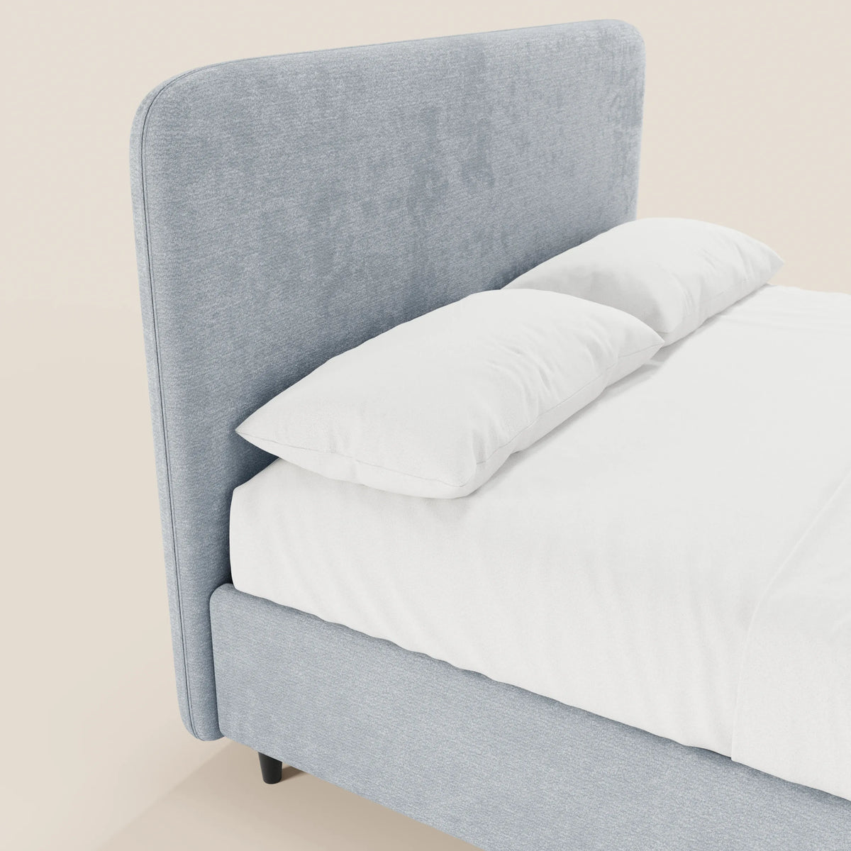 Un primo piano del letto KAELOS minimal imbottito di Letti.store, caratterizzato da una testiera curva rivestita in morbida ciniglia, gambe alte e vano contenitore. Il letto, dalle linee curate, è rifinito con lenzuola bianche e due grandi cuscini su uno sfondo neutro.