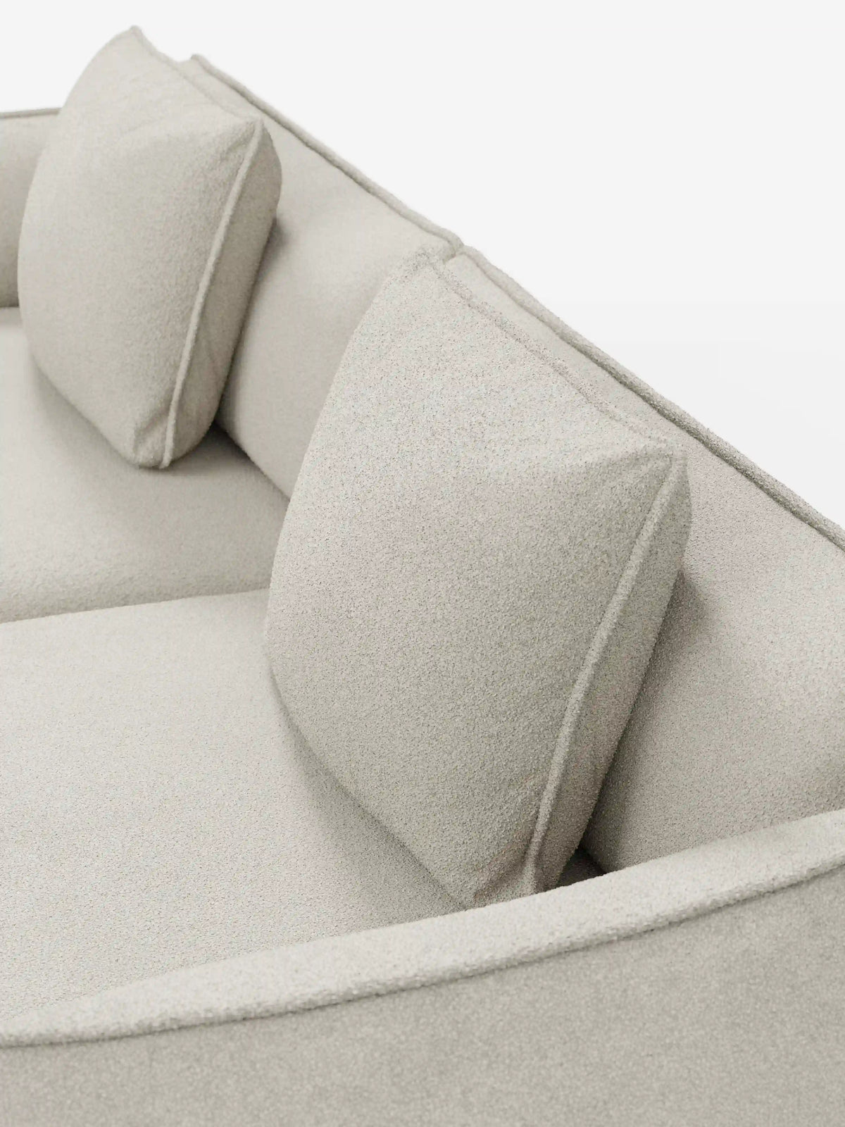 Un primo piano del divano modulare e componibile a 3 posti Nimbus da 250 cm di divitt.sbs, un elegante divano modulare beige chiaro rivestito in tessuto smacchiabile effetto cotone T33. Questo modello sfoderabile presenta due cuscini quadrati coordinati per lo schienale, linee pulite e minimaliste e una seduta morbida con rivestimento testurizzato che unisce eleganza e praticità, il tutto su uno sfondo bianco.