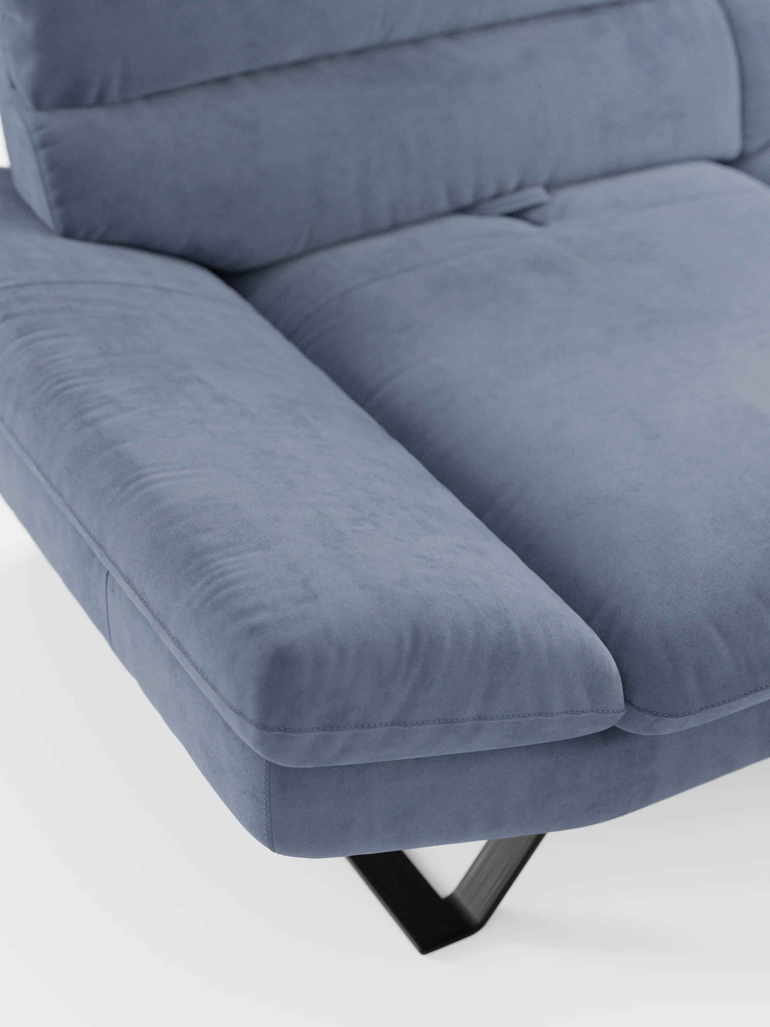 Primo piano del divano Eclipse, dal design moderno, a 2 e 3 posti con schienali traslanti, di divitt.sbs, rivestito in morbida microfibra T11 smacchiabile di colore azzurro chiaro. Si notano chiaramente l’ampio bracciolo e il cuscino di seduta, con eleganti gambe alte in metallo nero che spuntano parzialmente da sotto. Dotato di seduta modulabile per un maggiore comfort e flessibilità, la superficie liscia e morbida risalta sullo sfondo bianco.