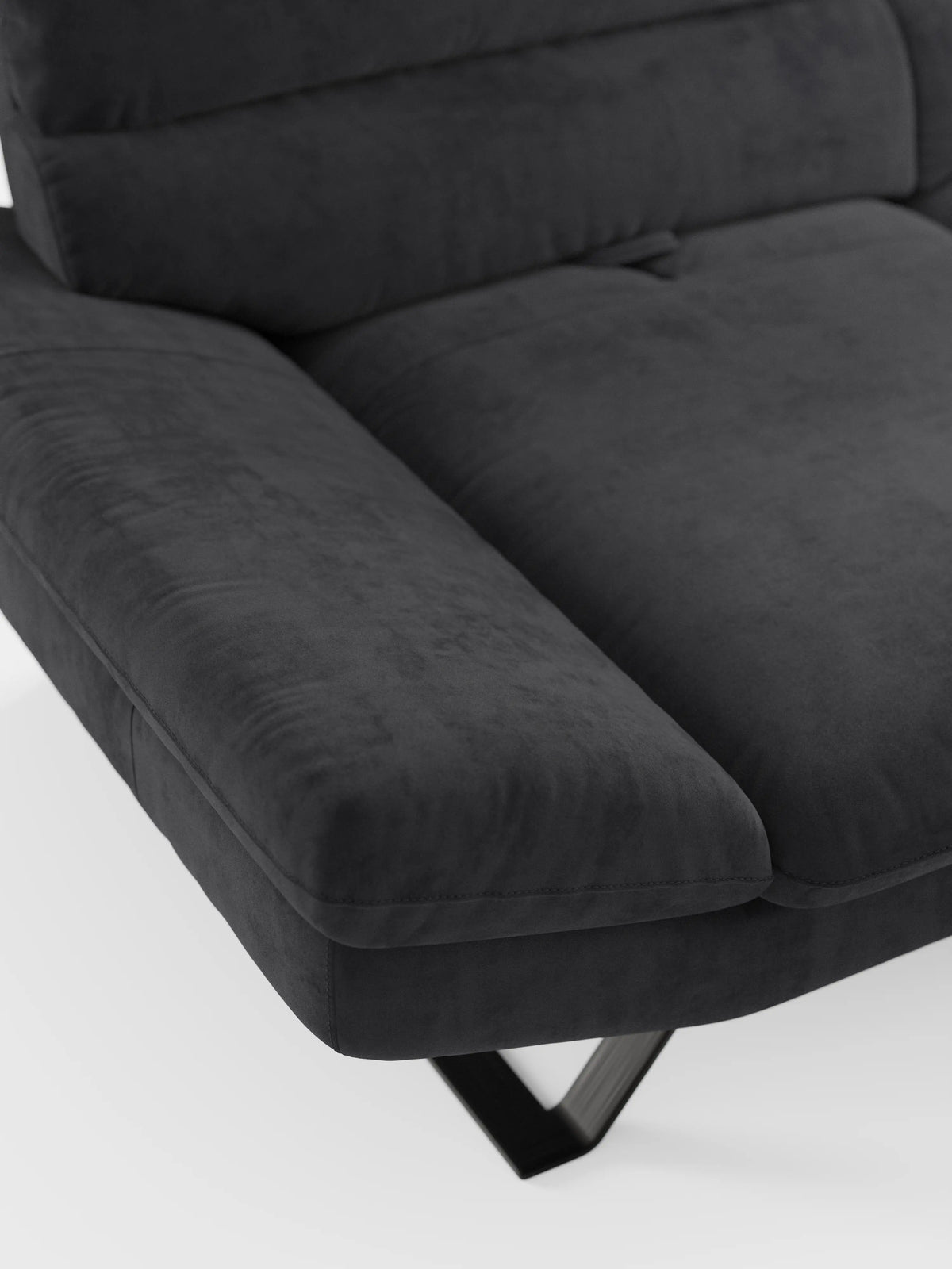 Primo piano del divano Eclipse, un modello moderno a 2 e 3 posti con schienali scorrevoli di divitt.sbs, rivestito in elegante microfibra T11 resistente alle macchie. Questo divano contemporaneo color grigio scuro presenta braccioli ampi e imbottiti, cuscini morbidi e piedini alti ed eleganti in metallo nero. La trama del rivestimento è chiaramente visibile, sottolineando una sensazione di morbidezza e comfort modulabile. In primo piano su uno sfondo bianco a tinta unita.