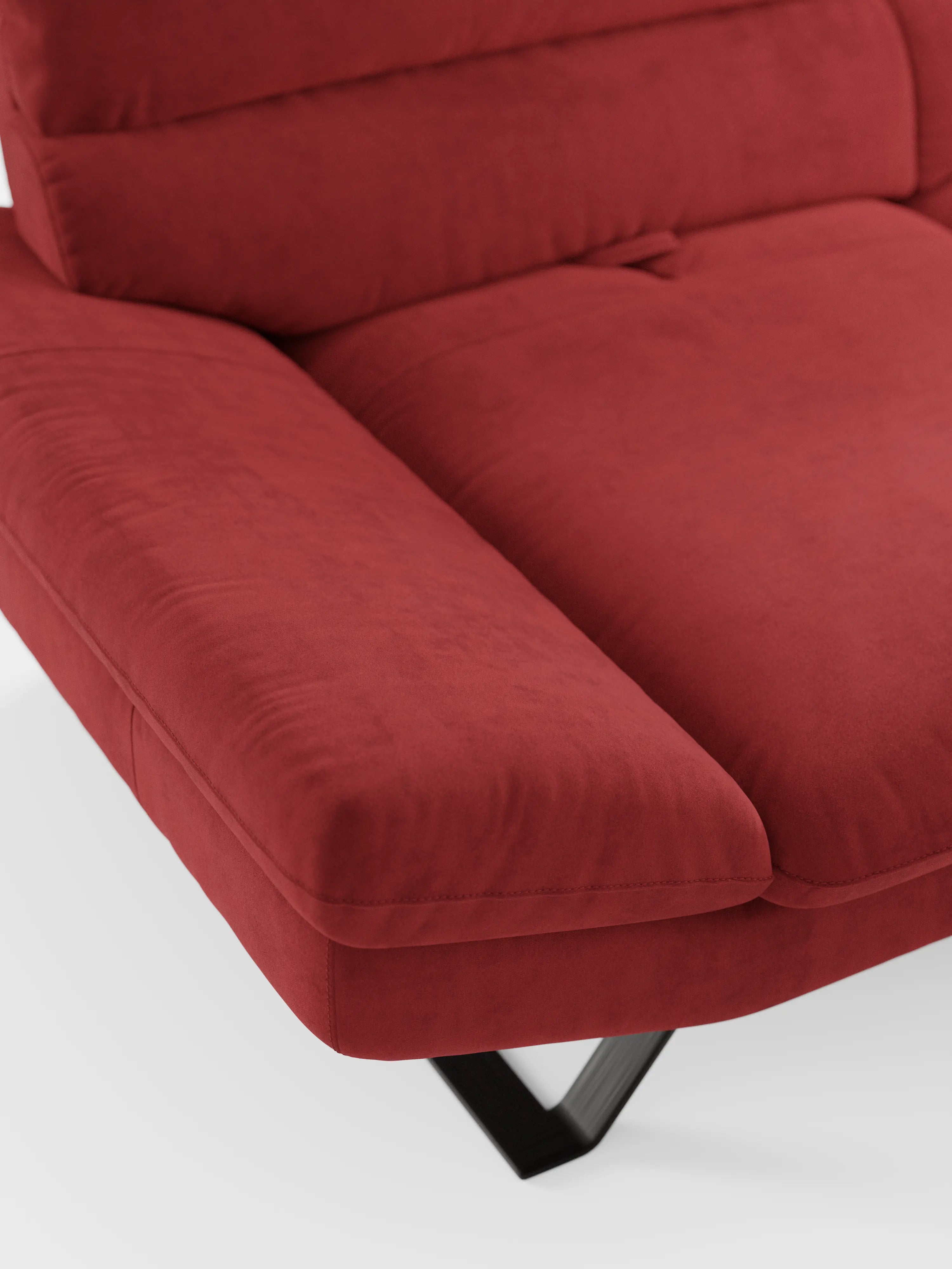 Primo piano del divano Eclipse dal design moderno a 2 e 3 posti di divitt.sbs in un rosso vivace, rivestito in elegante microfibra smacchiabile T11 resistente alle macchie. Il divano è caratterizzato da ampi braccioli imbottiti e da schienali traslanti per un comfort personalizzabile e modulabile. La sua gamba angolare in metallo nero poggia su un pavimento bianco, mentre l’immagine si concentra sul dettaglio dell’angolo per mettere in risalto la texture morbida e l’estetica contemporanea.