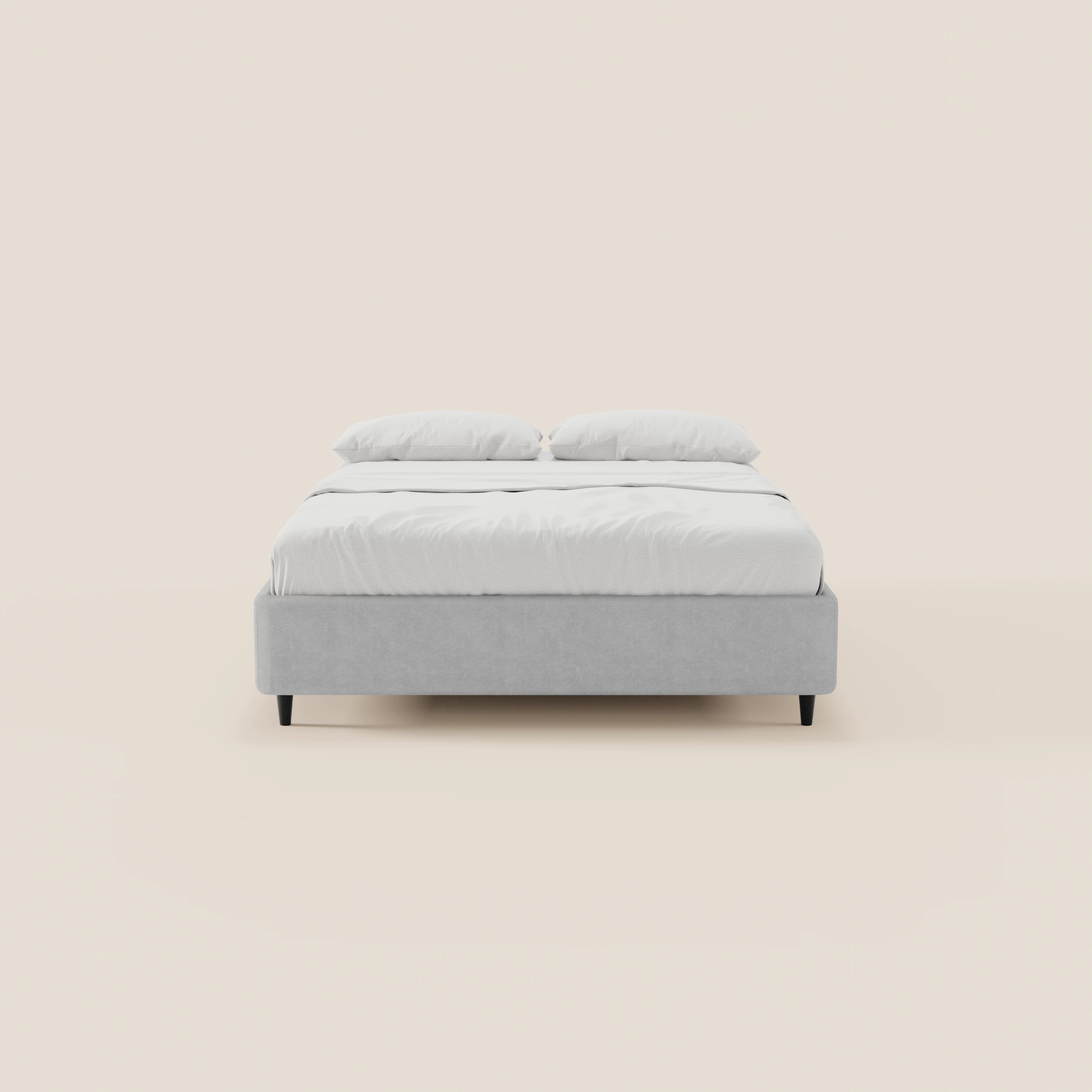 Il letto sommier imbottito ERON di Letti.store presenta una struttura in tessuto impermeabile grigio chiaro certificato Oeko-Tex, gambe nere e un materasso bianco con due cuscini, il tutto su uno sfondo beige a tinta unita che conferisce al letto un look moderno.