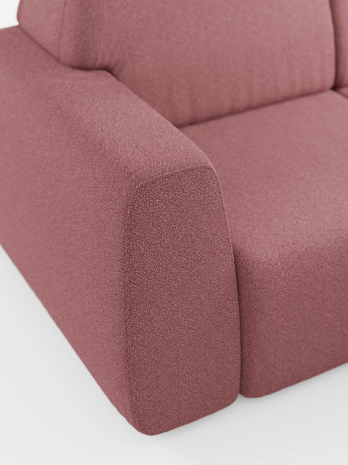 Primo piano del divano angolare Orbit con penisola reversibile e tutte le sedute allungabili di divitt.sbs, rivestito in tessuto effetto cotone (T33) color rosa polveroso testurizzato e resistente alle macchie. L’immagine mette a fuoco il bracciolo, la seduta e parte dello schienale, sottolineandone le linee pulite, la superficie liscia e il design minimalista — elementi distintivi dell’arredamento di alta gamma. Lo sfondo è una superficie bianca a tinta unita.