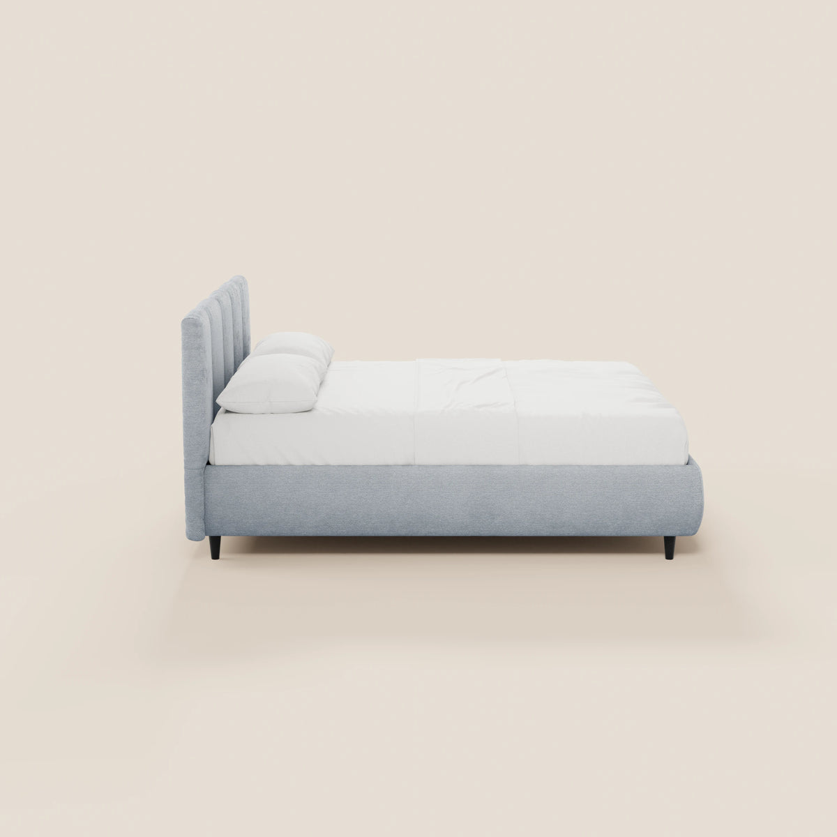 Il letto imbottito ARKAM di Letti.store presenta una struttura in tessuto grigio chiaro certificato Oeko-Tex® e una testiera con cuciture verticali, un lenzuolo con angoli bianco, due cuscini e gambe corte nere. Il suo design shabby chic risalta sullo sfondo beige a tinta unita.