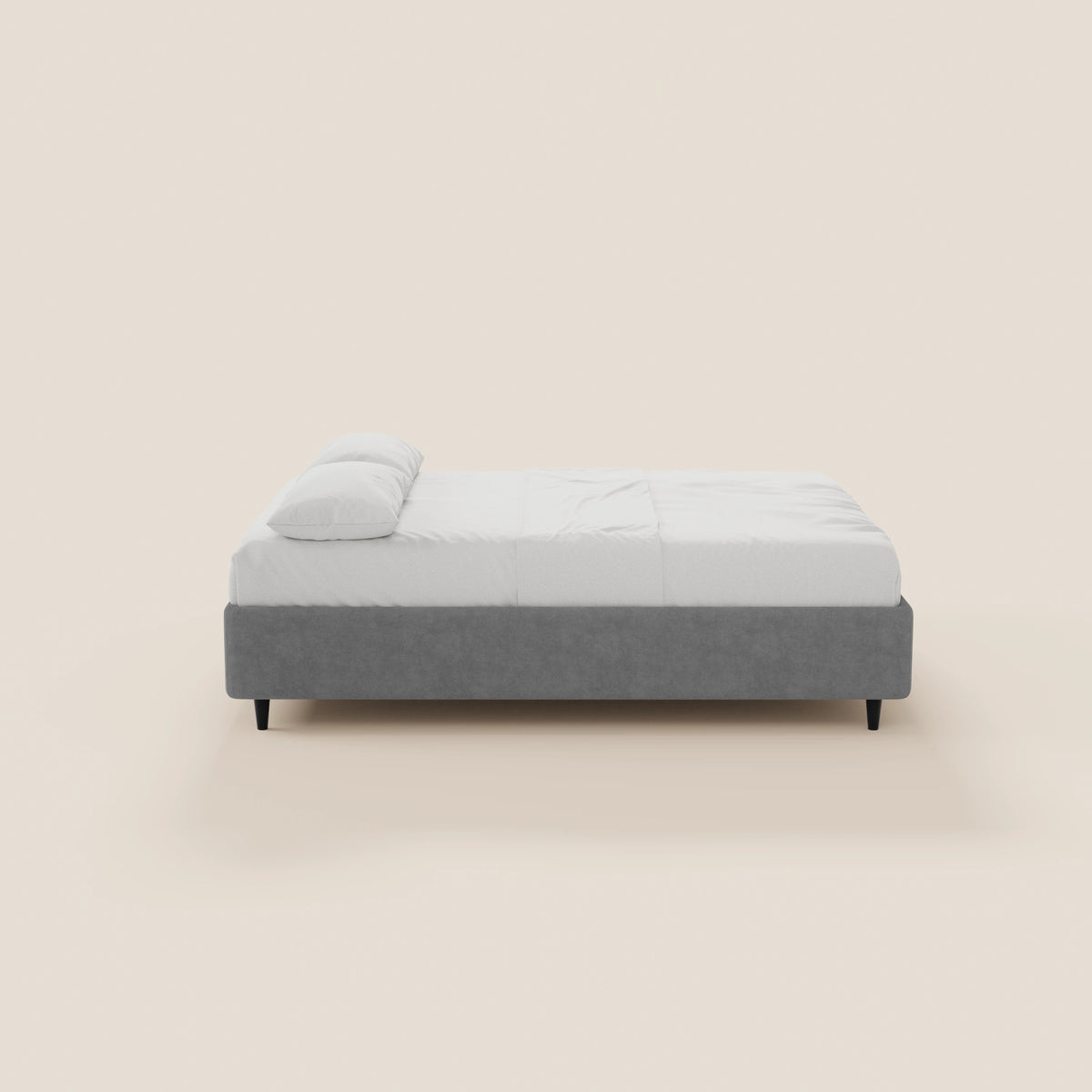 Una vista laterale del letto sommier imbottito ERON di Letti.store, caratterizzato da una struttura in tessuto grigio impermeabile certificato Oeko-Tex, lenzuola bianche e un cuscino bianco singolo su uno sfondo beige chiaro.