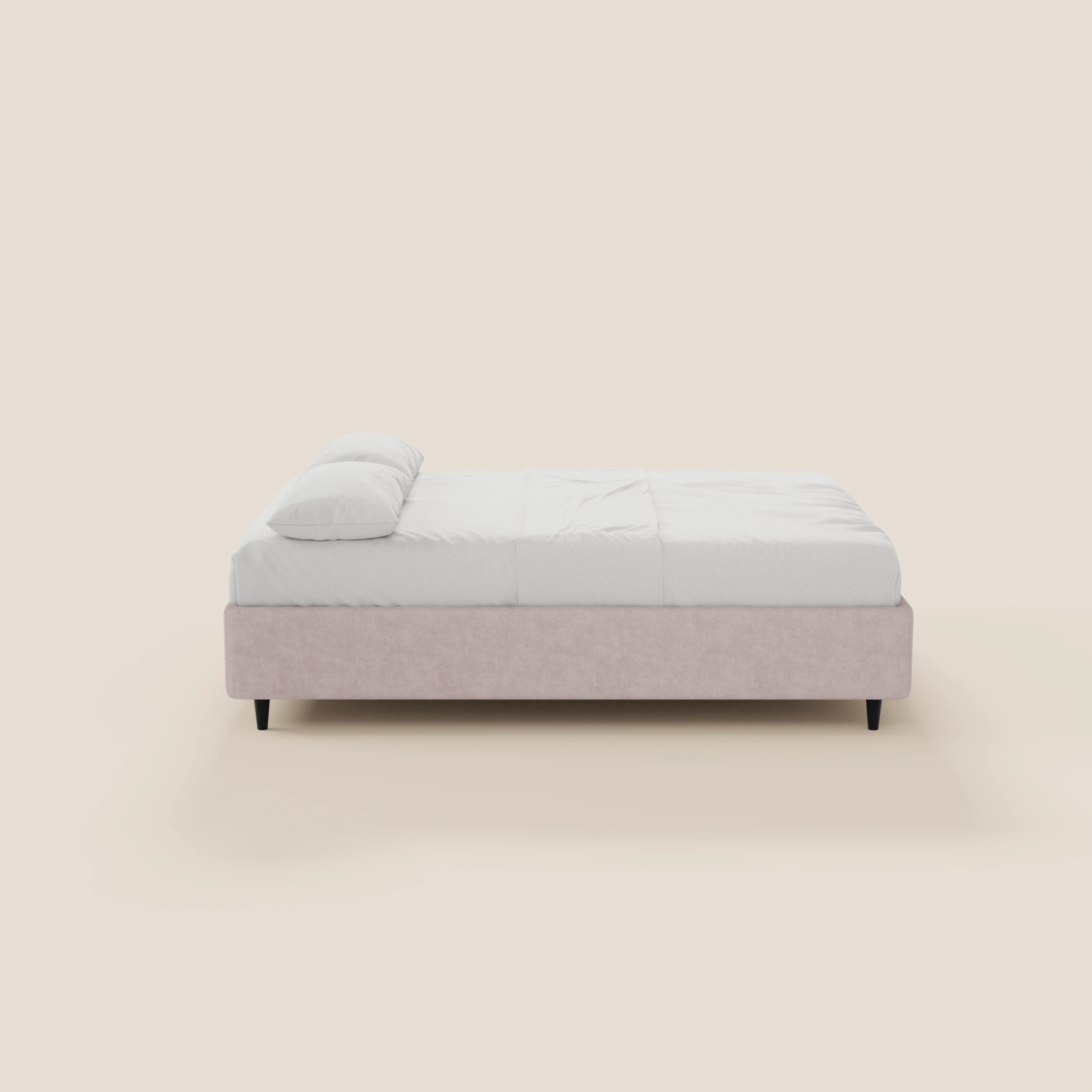 Il letto sommier imbottito ERON di Letti.store presenta un design moderno e dal profilo basso, con una struttura in tessuto impermeabile Oeko-Tex grigio chiaro, biancheria da letto bianca e linee minimaliste; nella foto è raffigurato di profilo su uno sfondo beige.