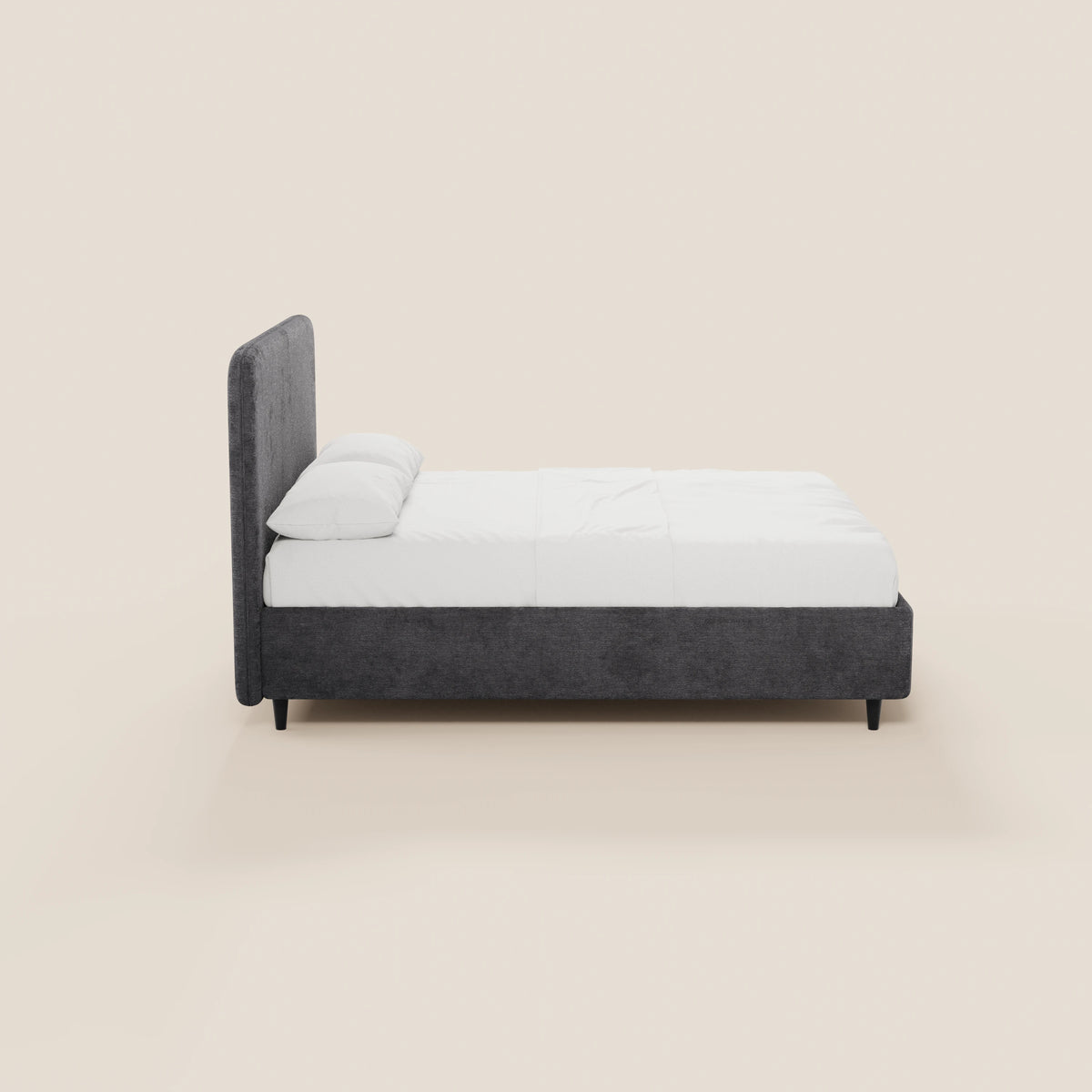 Una vista laterale del letto KAELOS minimal imbottito di Letti.store, con struttura rivestita in ciniglia grigio scuro, testiera arrotondata, biancheria da letto e cuscini bianchi, gambe alte nere e un vano contenitore, su uno sfondo beige chiaro.