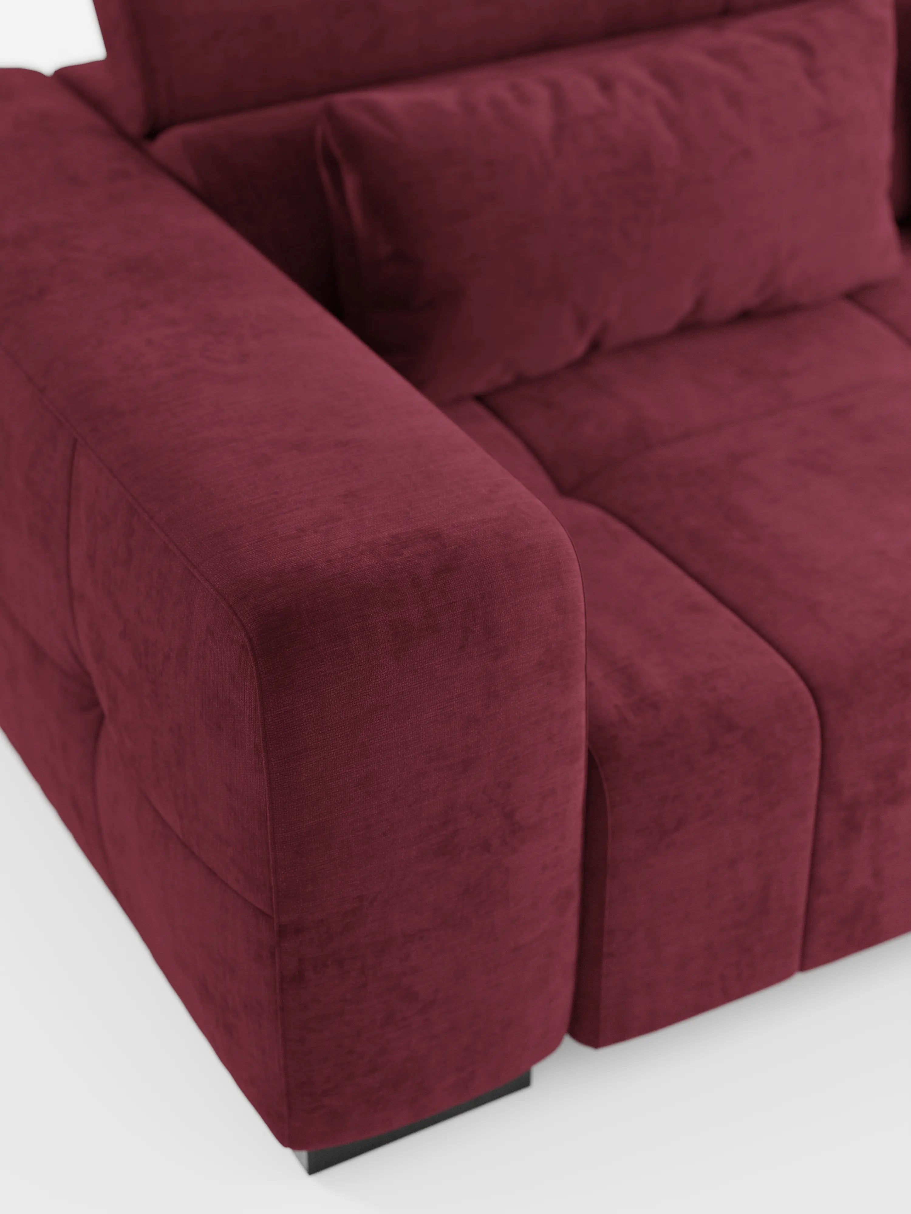 Primo piano del divano angolare Monarch con penisola e funzione Relax Elettrico per l'allungamento delle sedute di divitt.sbs, rivestito in tessuto T31 smacchiabile color bordeaux scuro. L'ampio e morbido bracciolo presenta cuciture a vista e una consistenza soffice. Sono visibili parte dello schienale regolabile con poggiatesta reclinabili e il cuscino della seduta, il tutto su sfondo bianco.